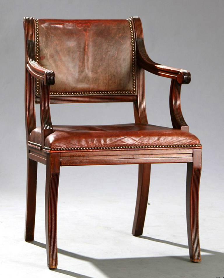 Large set of Regency-style armchairs, in mahogany, covered in red leather with reeded arms and legs. This set comprises 12 chairs but can be sold as a set of ten. Dating from the early 20th century, the leather is in used condition with good