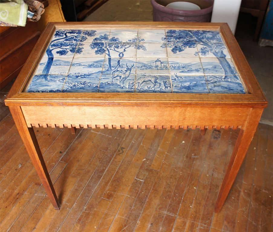 Danish tile top tea table in oak with dentil edges and blue and white tiled top, the top's design depicting deer and fauns in a pastoral landscape, by Danish designer Frits Henningsen c 1940's
      