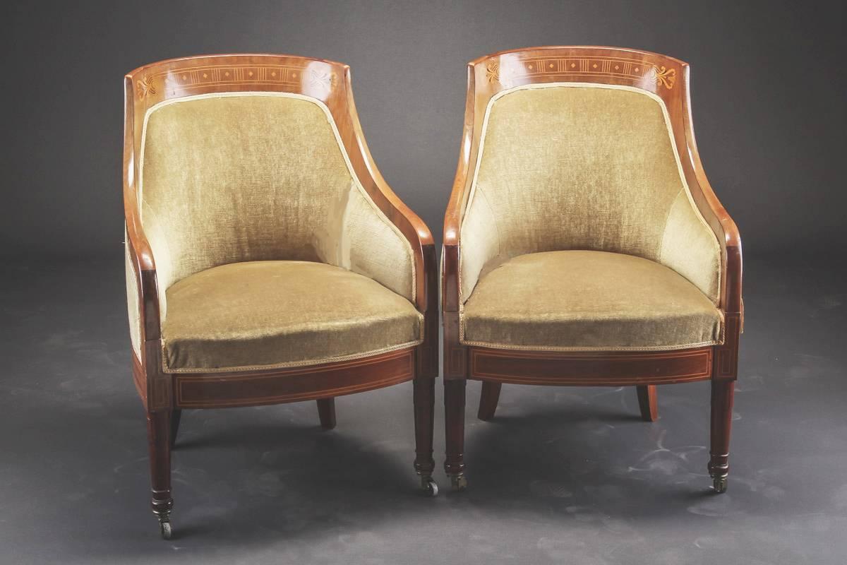 Pair of Swedish art deco mahogany gondola back bergeres with marquetry inlaid backs and inlaid stringing on legs. The chair's front legs mounted with casters. Note:  chairs should be reupholstered. The frames are in good condition with no losses to