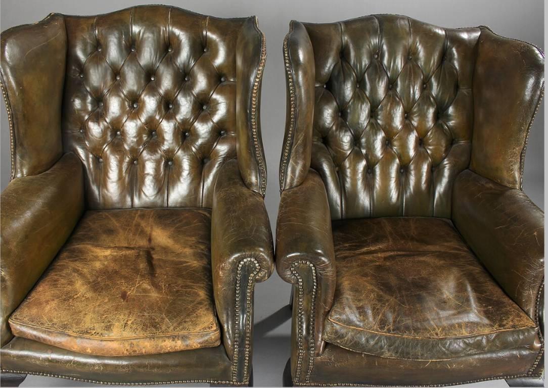 Pair of English George III style wing back armchairs with original close-nailed and button backed green leather upholstery.