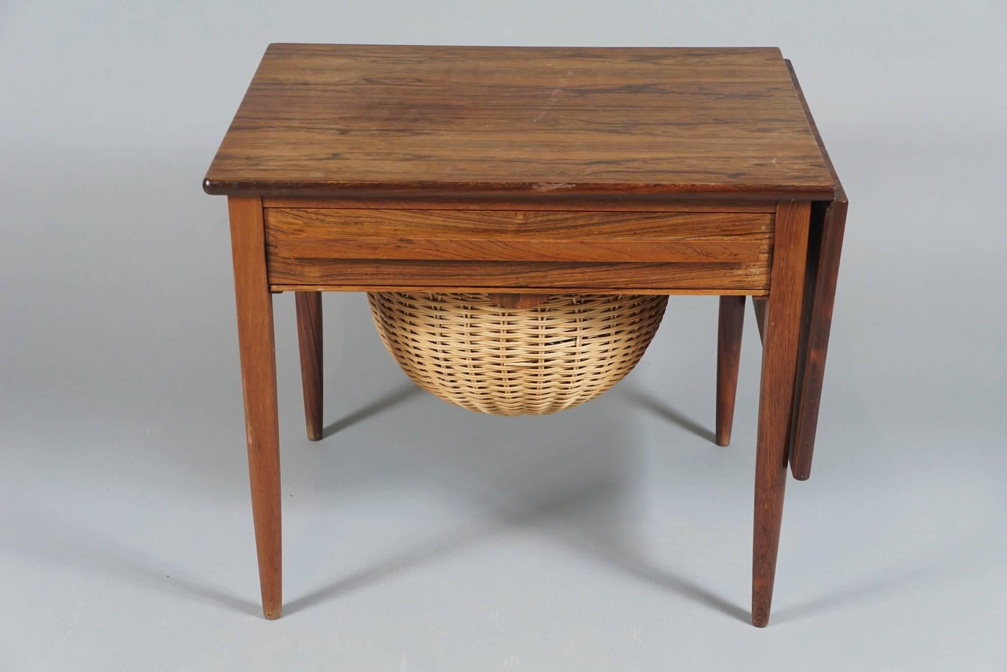 Unique Danish modern sewing table in finely figured rosewood, with sliding drop-leaf top, sewing article drawer and pull-out basket for wools, spools, etc. 
The table measures 36