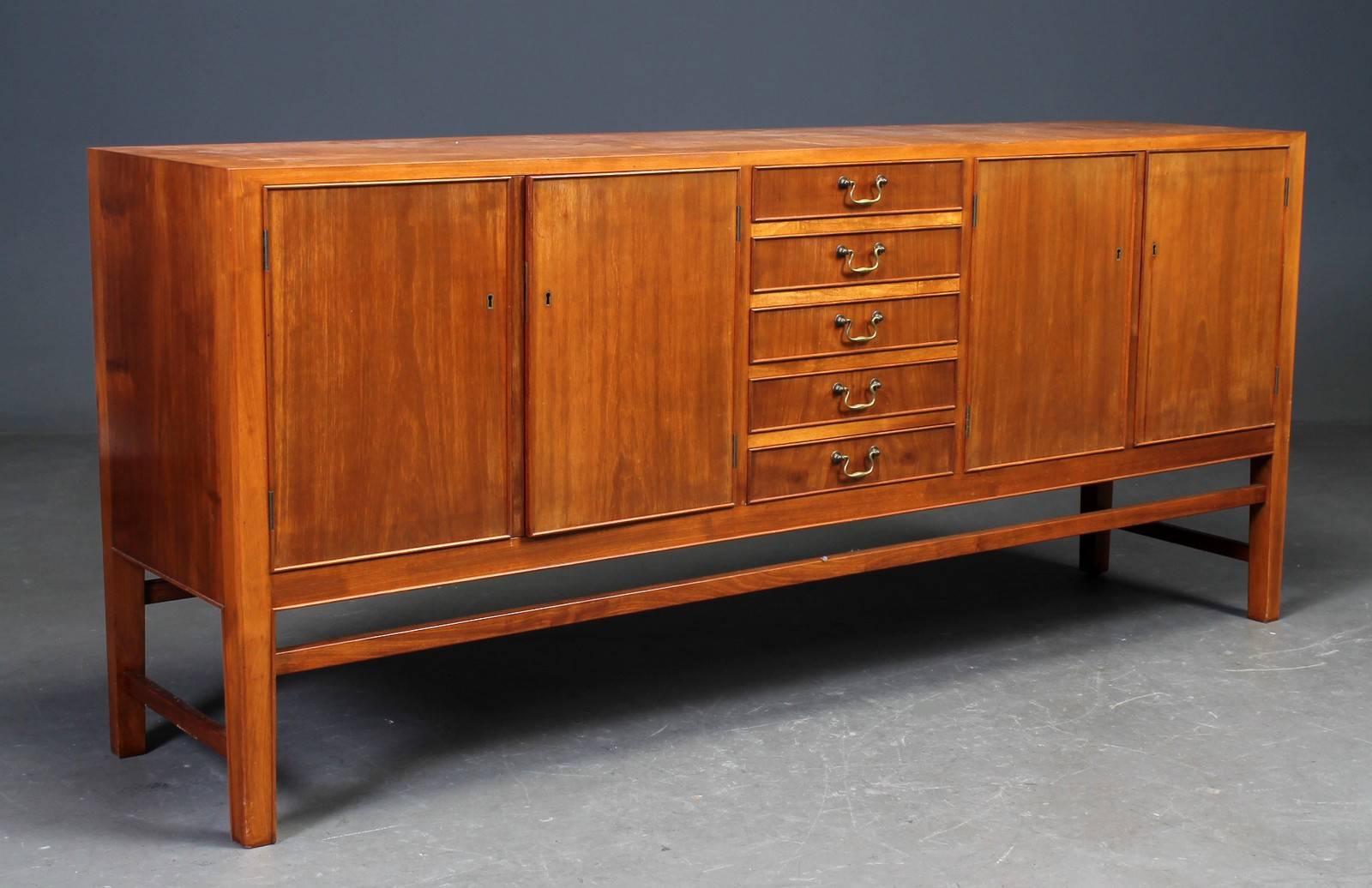 1940s Danish sideboard of Cuban mahogany. The front fitted with five pull-out baize lined drawers with brass handles with bronze finished mounts. The drawers with doors on each side opening to an interior fitted with shelves.