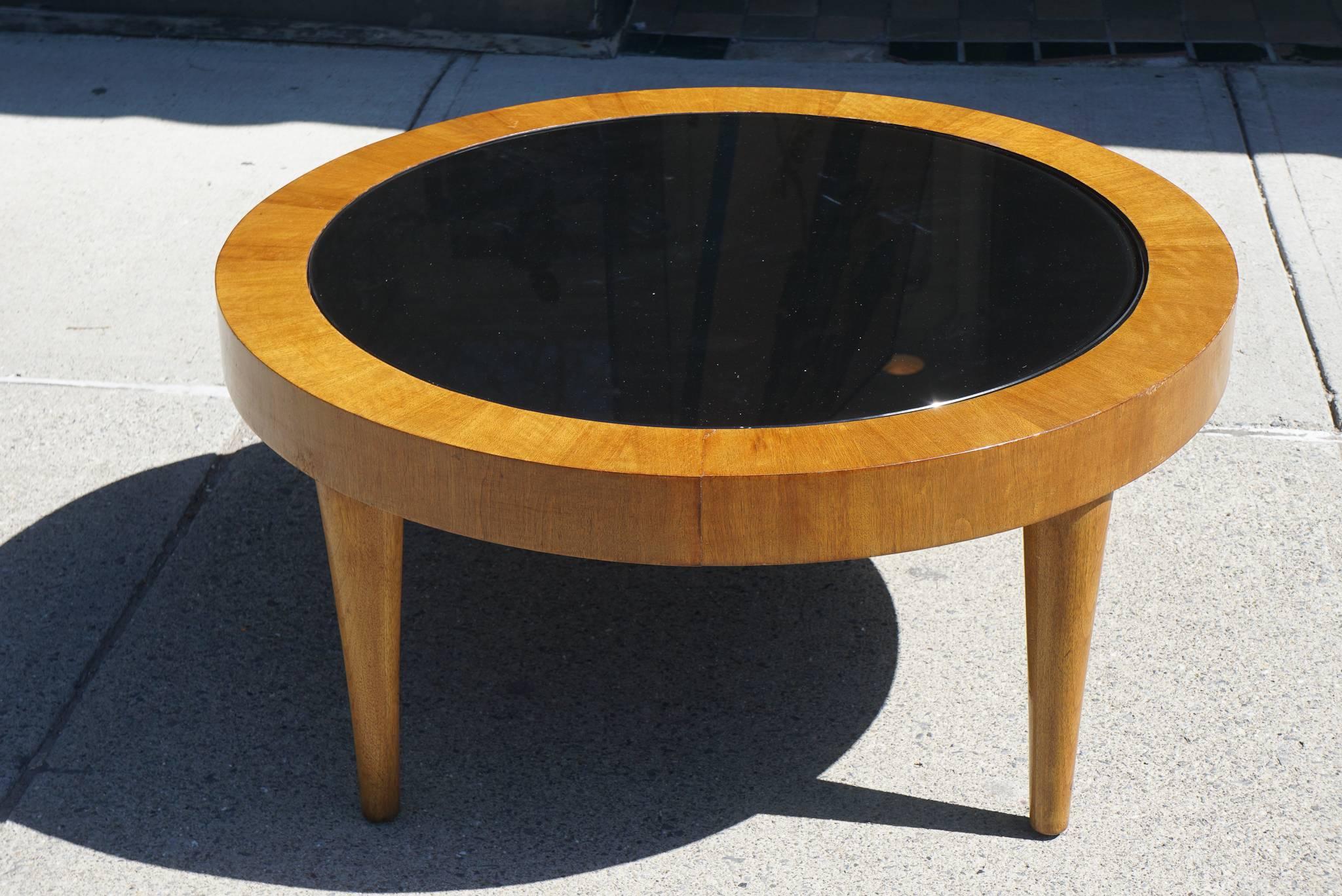 This modern vintage 1940s walnut coffee table is centered on a black glass top creating a dynamic play of light and dark contrasts. The wood grains are well-chosen to conform to the shape of the table creating a subtle play of lines. While simple in