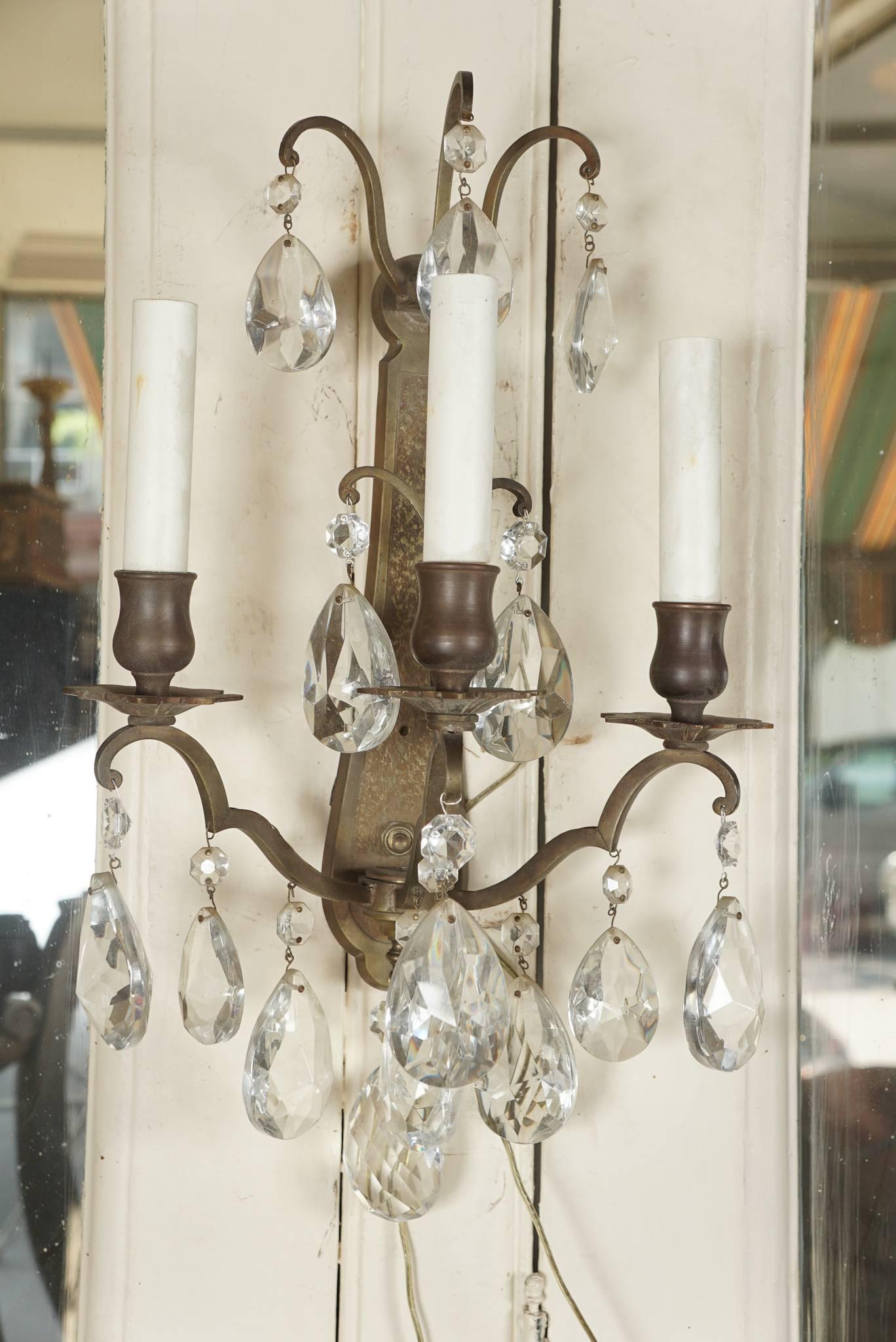 This pair of three-light scones made of cast bronze with an old world darkened patina were made in France and have been just rewired with American sockets and wiring. The pair made in the 1950s have large nicely cut crystal prisms in three different