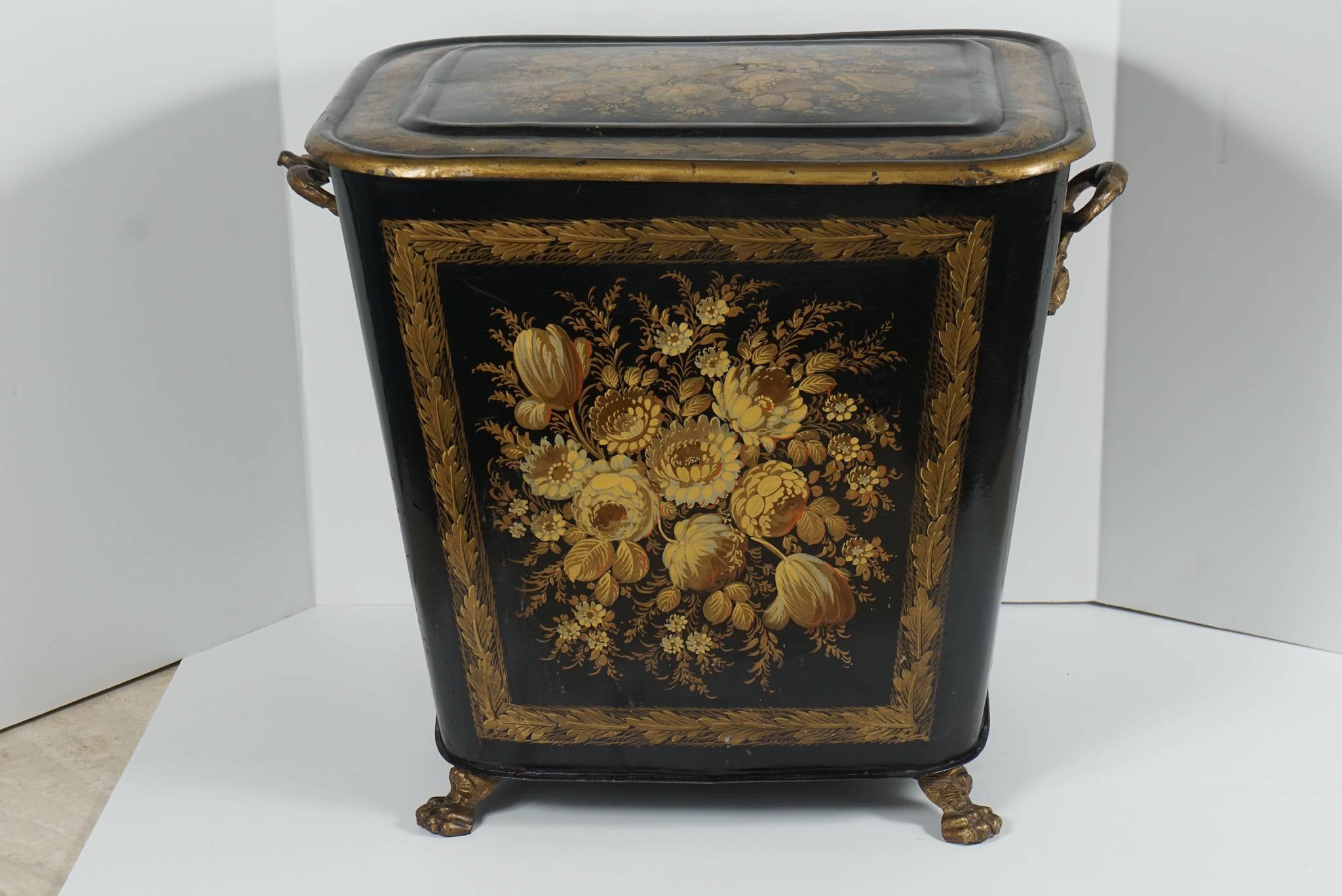 This tole pettie hamper made, circa 1850 in England shows a lovely design enlivened with fine paint details of floral sprays set within acanthus gilded borders on the top and front and back sides. Set in the upper area on the sides are two caring