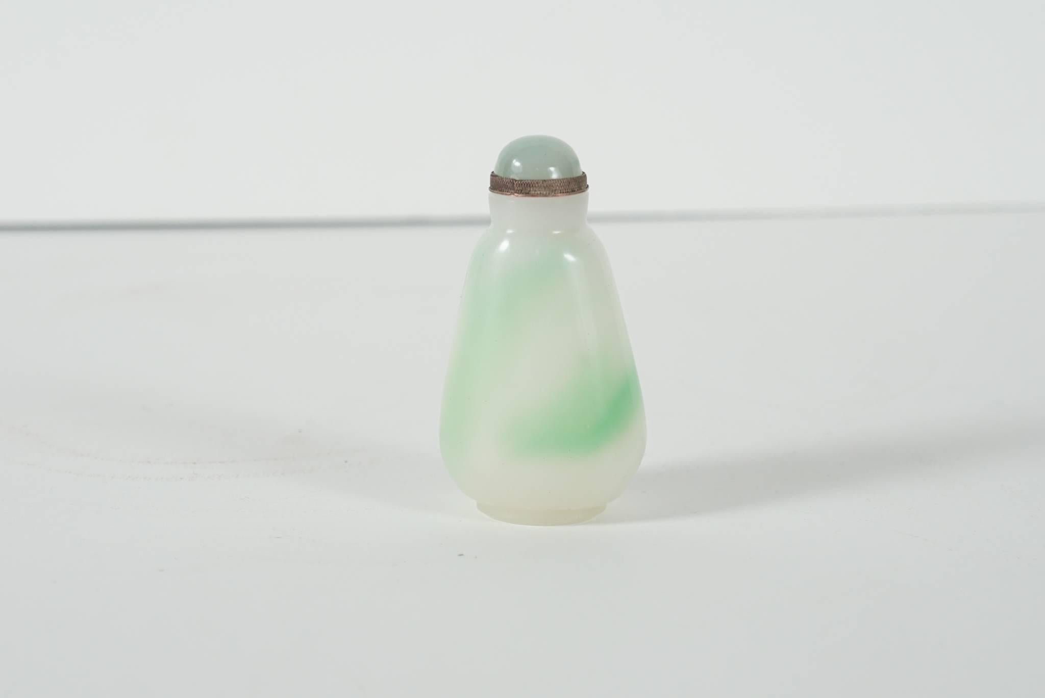 This small beautiful carved stone bottle carved from a piece of jadeite that runs from a white to an emerald green is Chinese and comes from the late 19th century to the Republic Period of China’s history. The lid is set in copper alloys that have