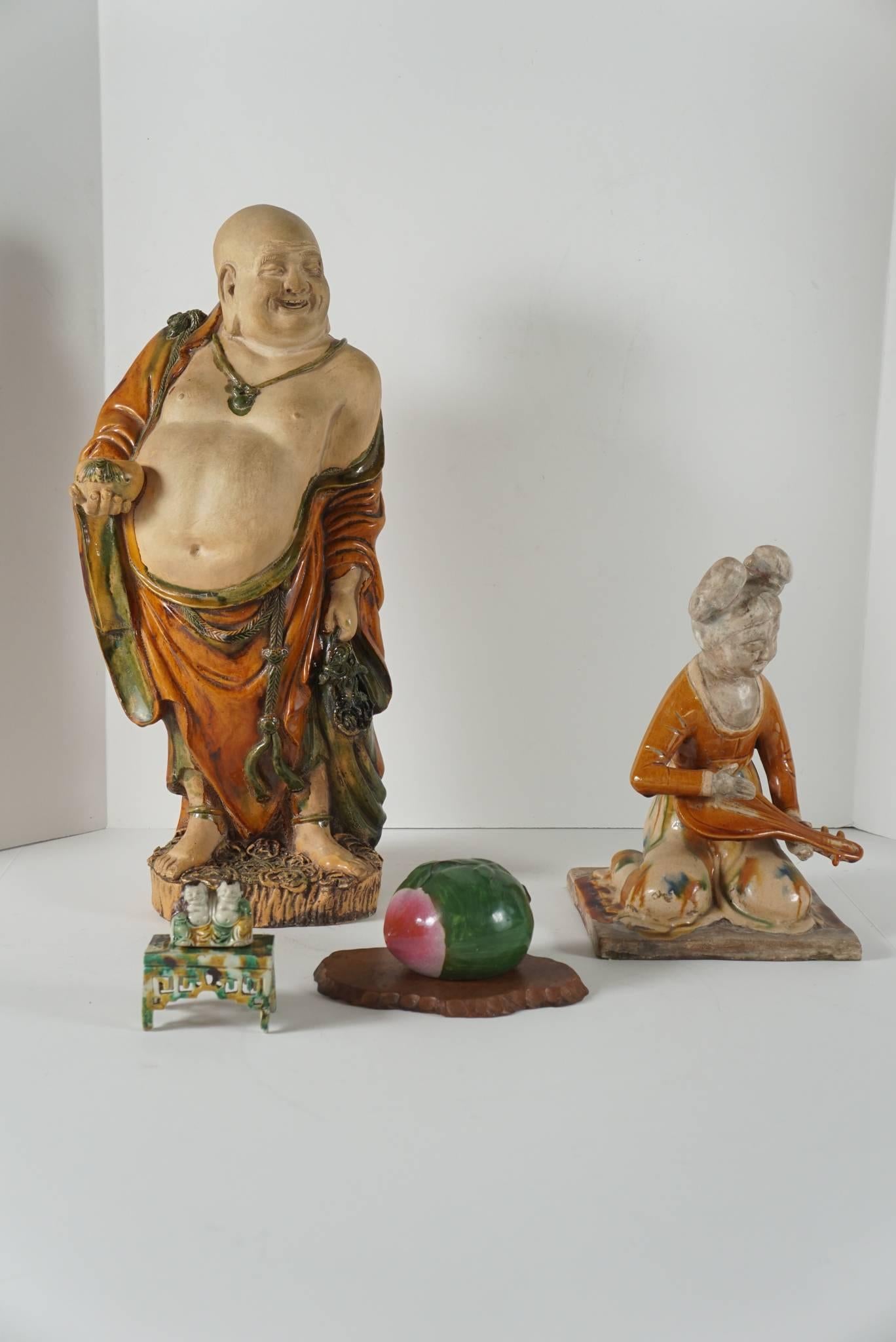 This collection includes a large standing Buddha holding a bowl wearing flowing draped robes, a Tang style kneeling figure of a court musician, a very nice small group of pot bellied figures set on a separate stand with a pierced apron and a single