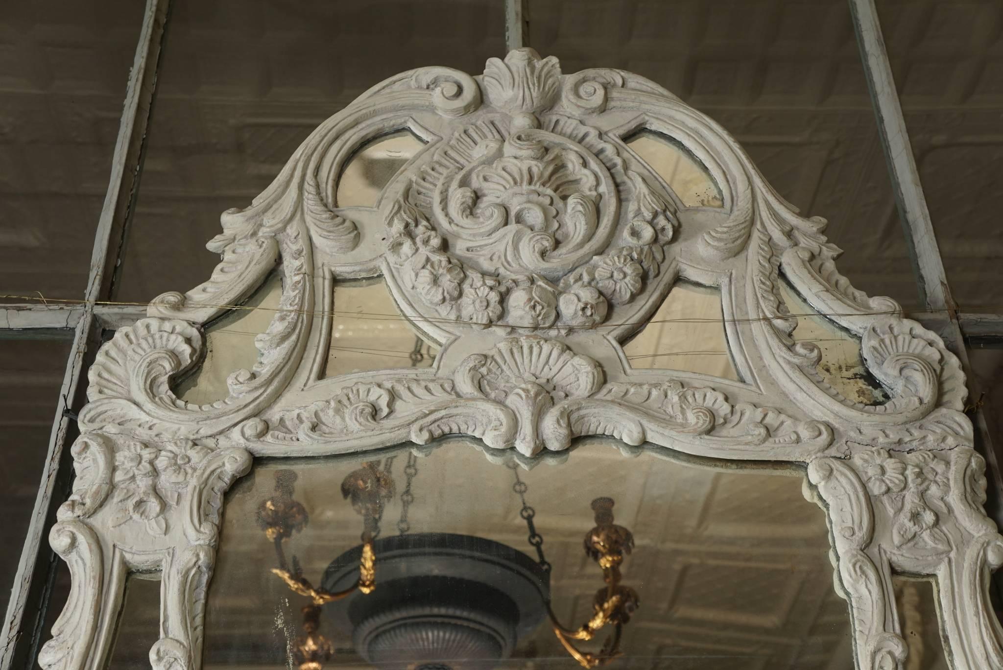 The large well-shaped frame with numerous openings showing mirror set behind, circa 1740. The frame is carved to depict cartouches composed of foliate borders and vining elements. These are made up of many s and c curved sections which will become