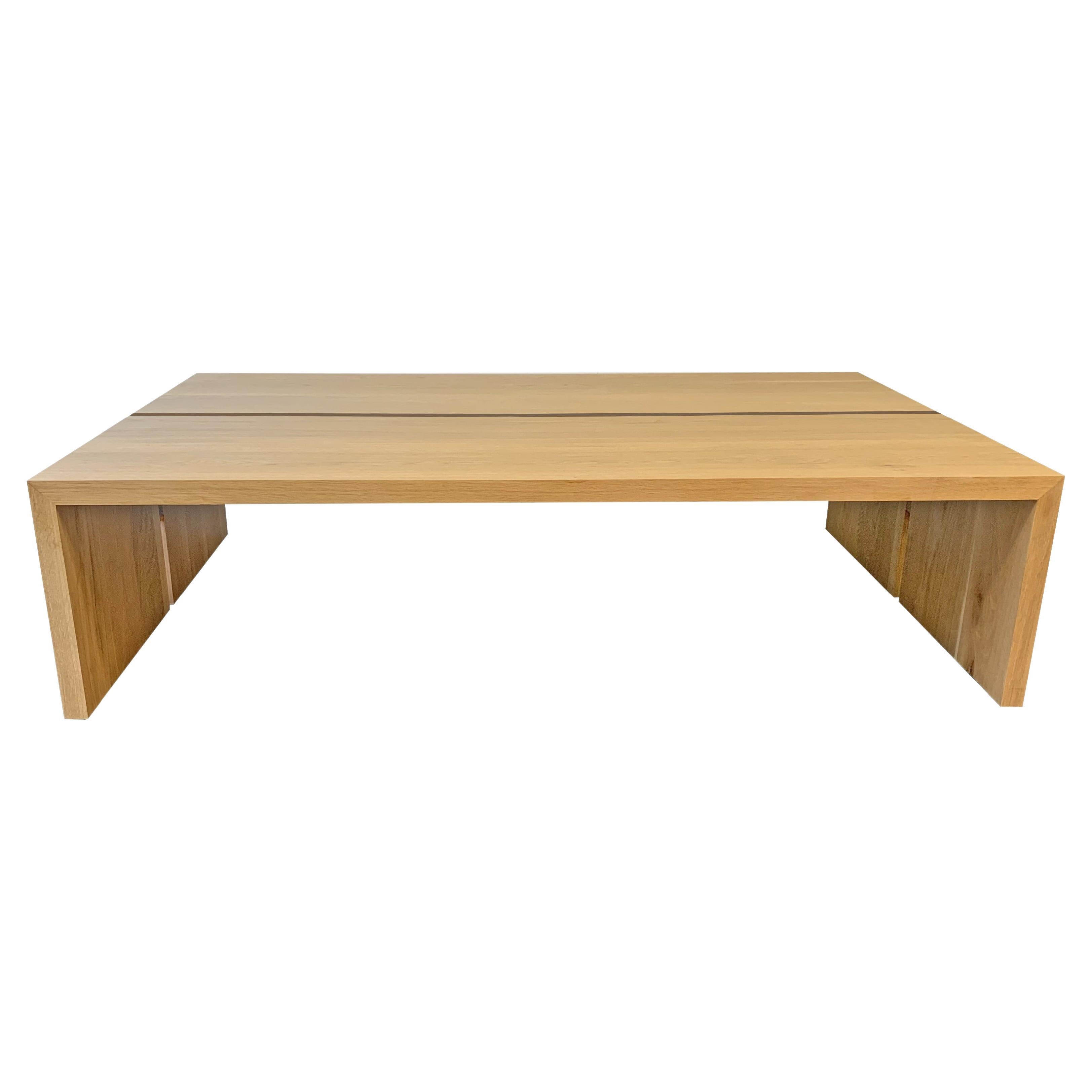 Cette table basse personnalisée est fabriquée à la main aux États-Unis avec du bois dur. Il présente un design moderne de cascade rectangulaire avec un corps en chêne blanc massif et un détail minimaliste d'incrustation en noyer. Les extrémités en