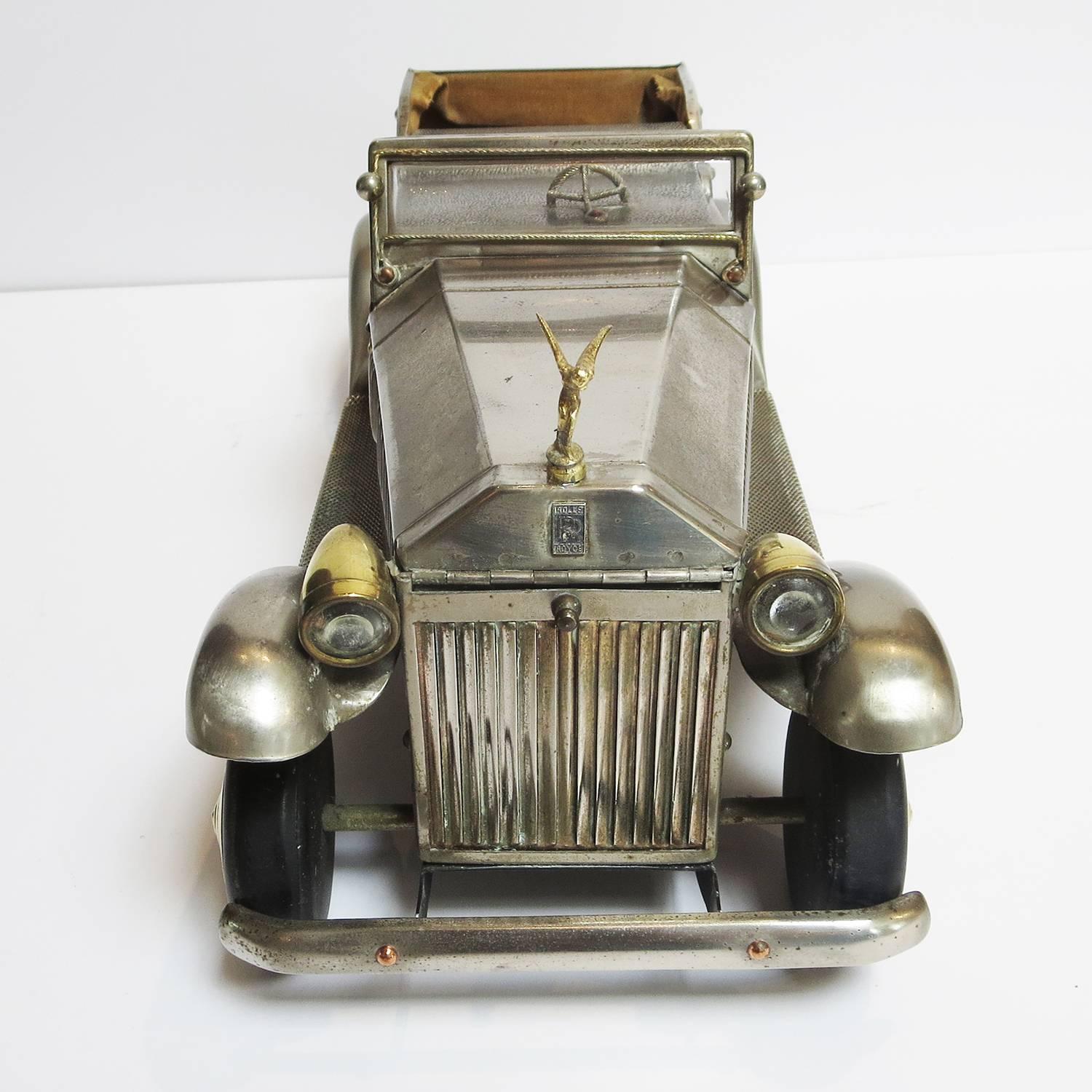 This charming jewelry box is crafted in the image of a classic 1930's Rolls Royce convertible. The car is finished in a satin nickel tone, with golden brass accents. The hood lifts up from the windshield, and is slotted for rings or cufflinks. The