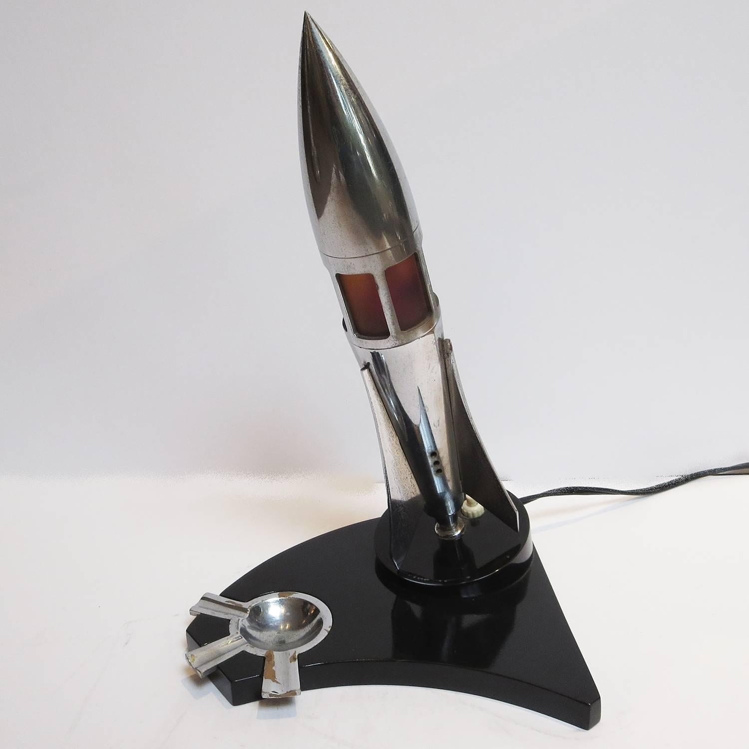 Smoking in style! This great desk top rocket features a small lamp through the red windows, and a small chromed ashtray. The base is black lacquered wood in excellent condition. The chrome elements show minor wear.