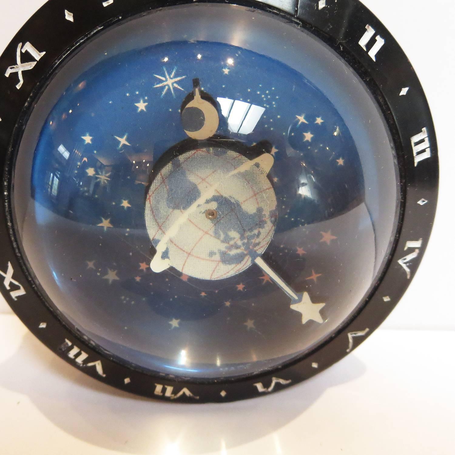 One of the most charming clocks made! This winding clock features a black bakelite case, and a thick glass dome. The world and star turn as a minute hand, white the crescent moon represents the hour hand. The clock face is a shimmering array of