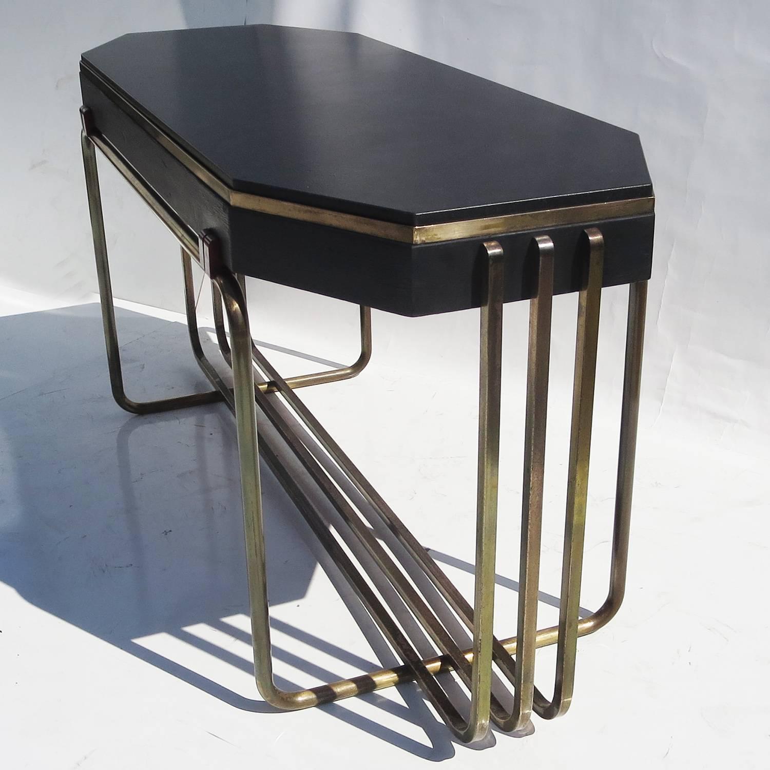 An exceptional design utilizing a base of intersecting square and round bronze tubing. The top is an octagon shaped painted wooden form, lifted off the tubes by four red catalin (bakelite) decorative blocks. A newly cut black granite top is set into