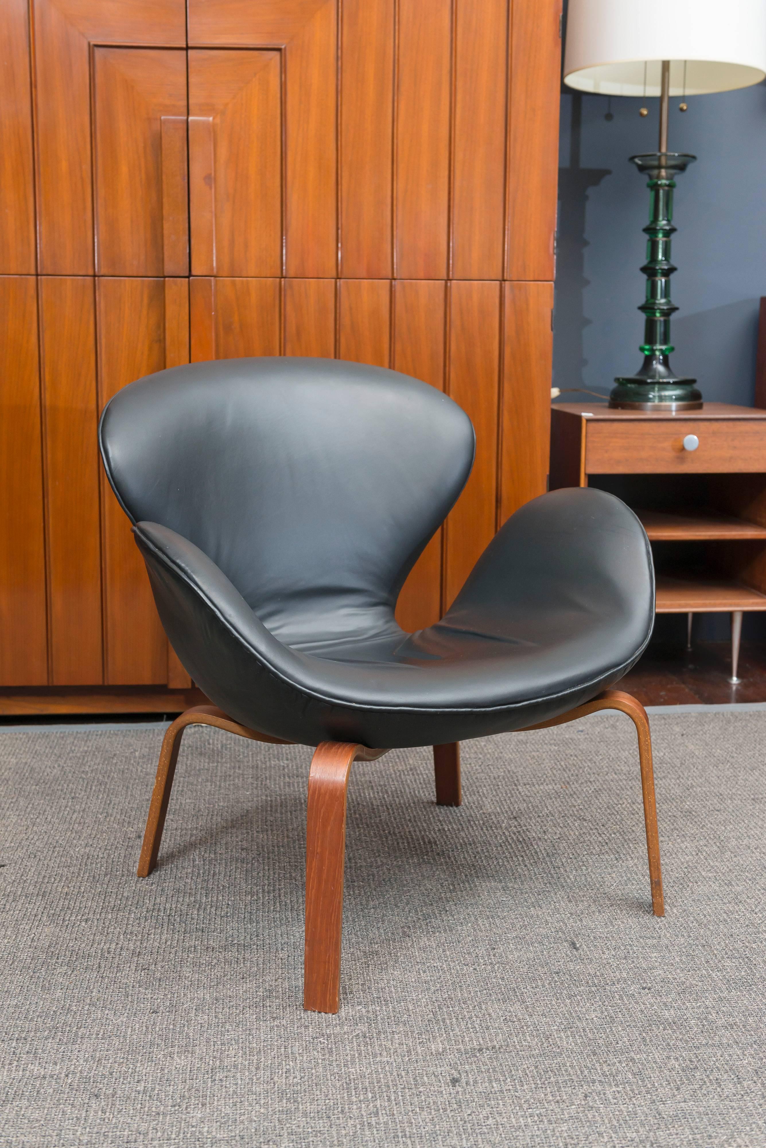 Early and rare version of Arne Jacobsen's iconic Swan chair for Fritz Hansen, Denmark. Newly upholstered in black leather on a moulded teak base, stamped.