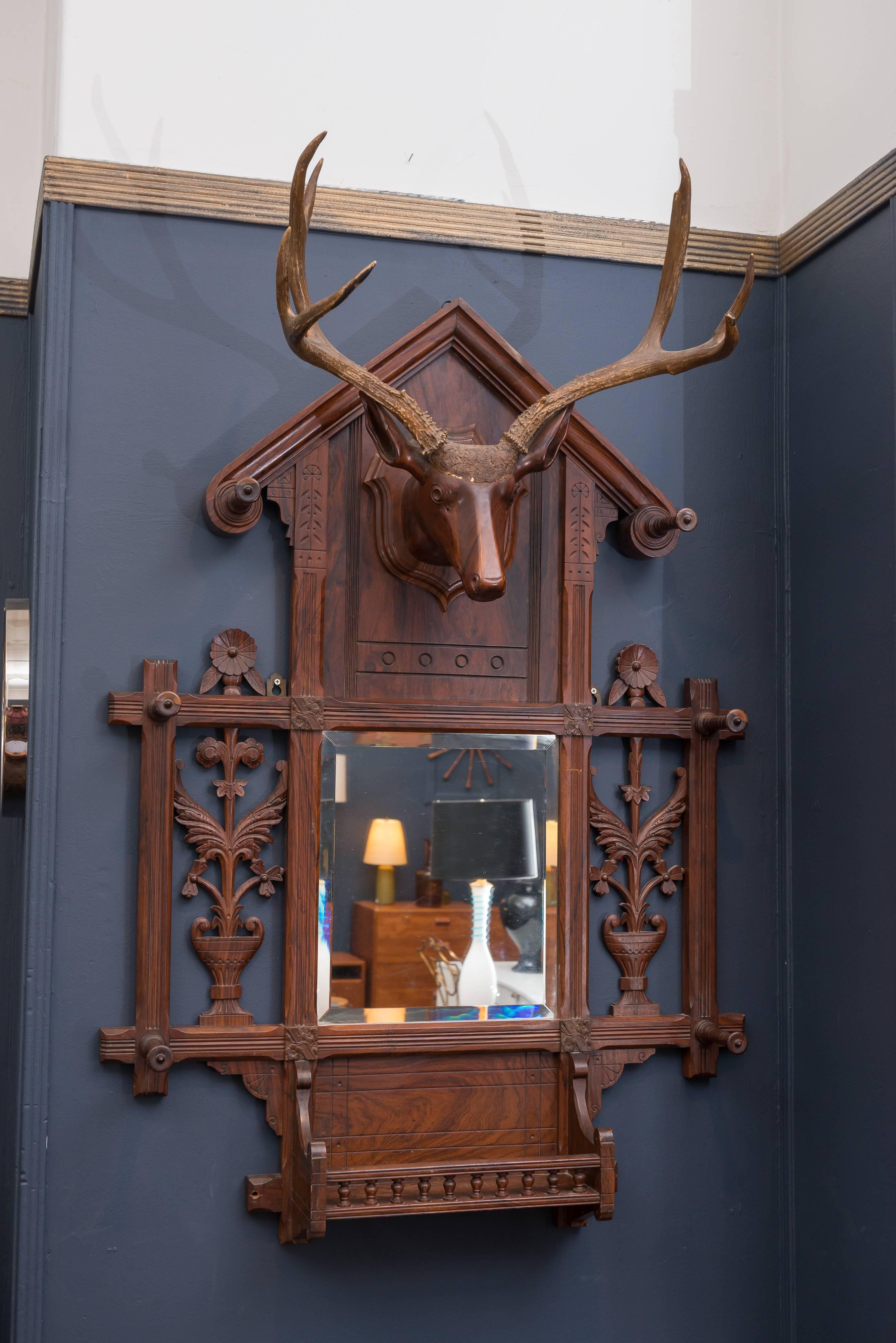 Black Forest handmade hall tree made from mahogany and rosewoods. Dramatic wooden carved deer head with antlers and floral carvings and hooks. Old repair to center of frame, original mirror plate.