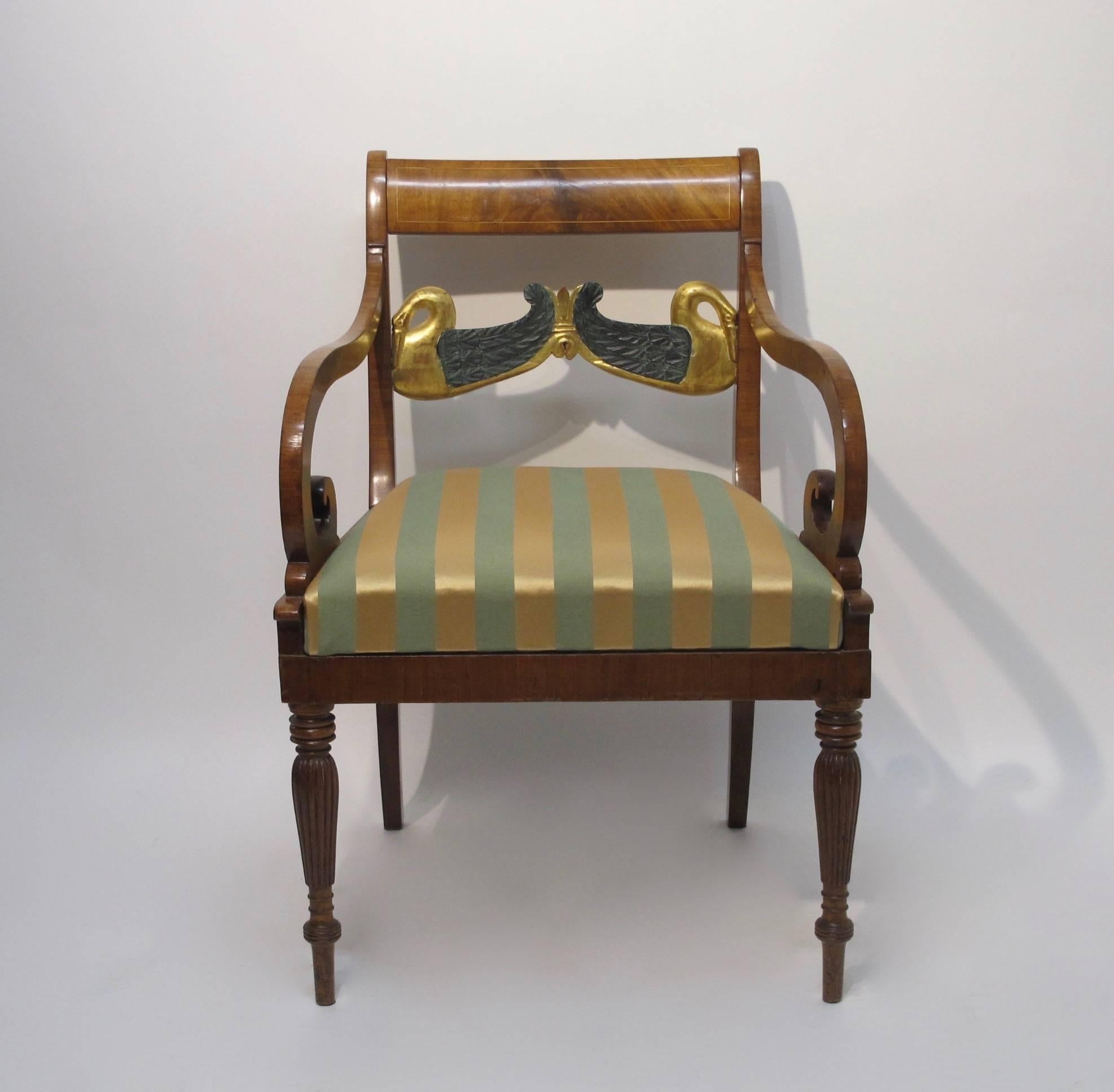A stylish mahogany armchair with gilt and parcel painted swan backs plat, gently swooping and curved arms, sitting on turned and reeded front legs with saber back legs. England, mid 20th century.