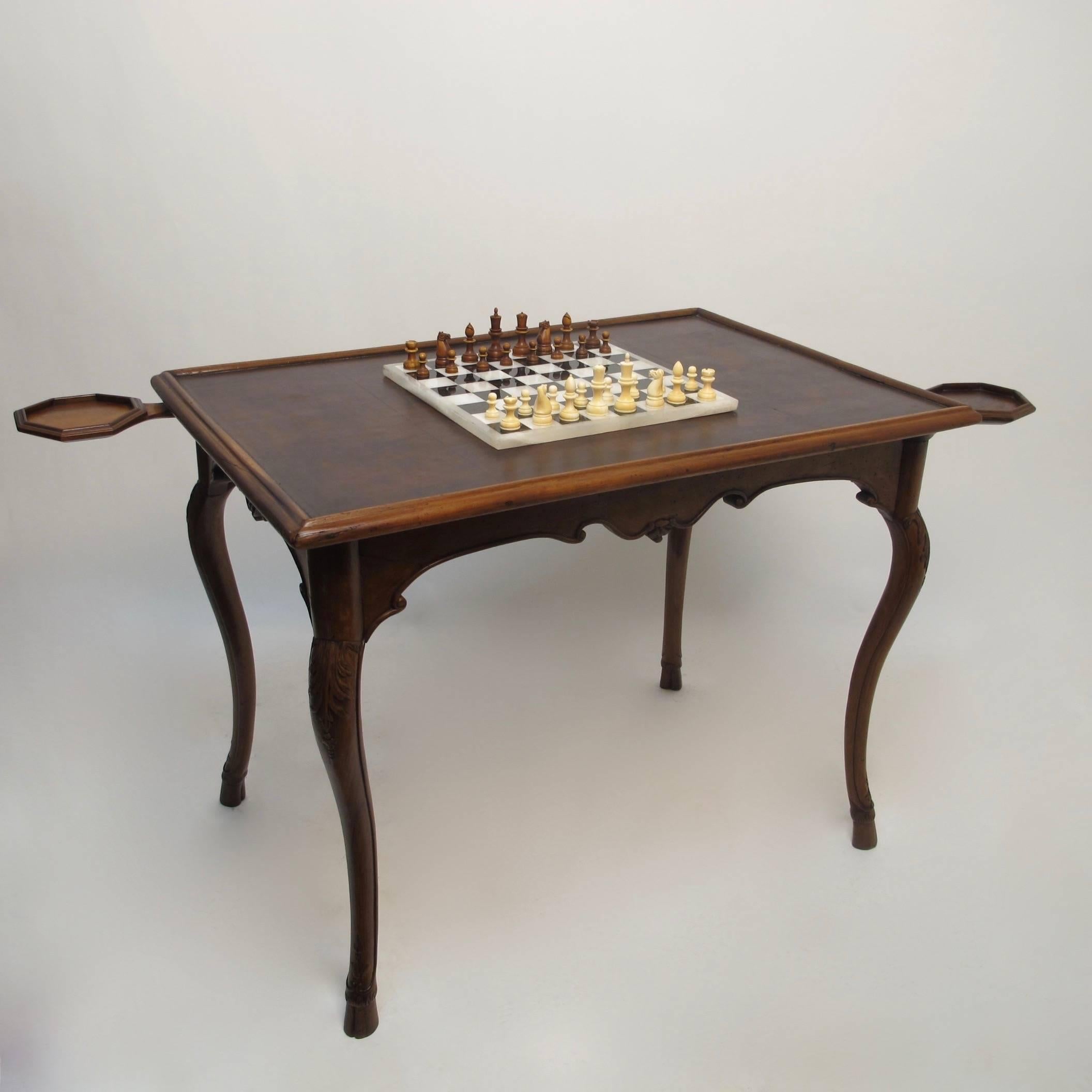 Beautifully carved walnut game table with inset leather top. Having a shapely apron, sitting on cabriole legs with carving at knees and ending with cloven hoof detail. The swing out cup or candle holders were most likely added in the mid-20th
