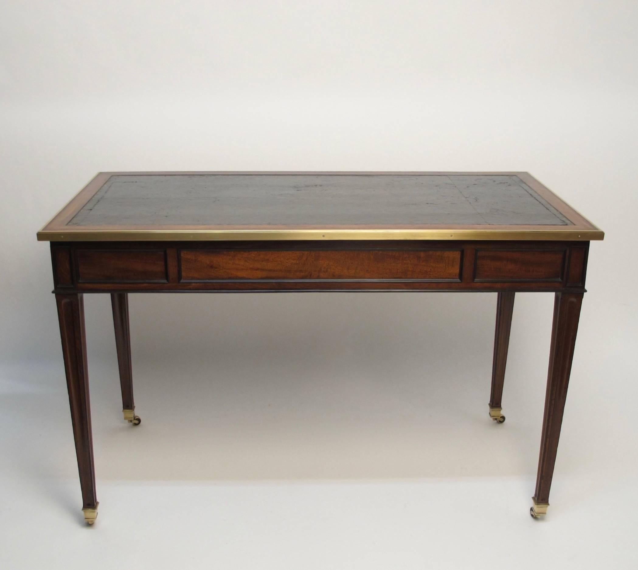 Mahogany writing desk with inset green leather top having gilt embossing and brass trim. Two short drawers flanking center drawer with ebonized moldings, tapering fluted legs ending in brass sabots with casters, France, circa 1880.