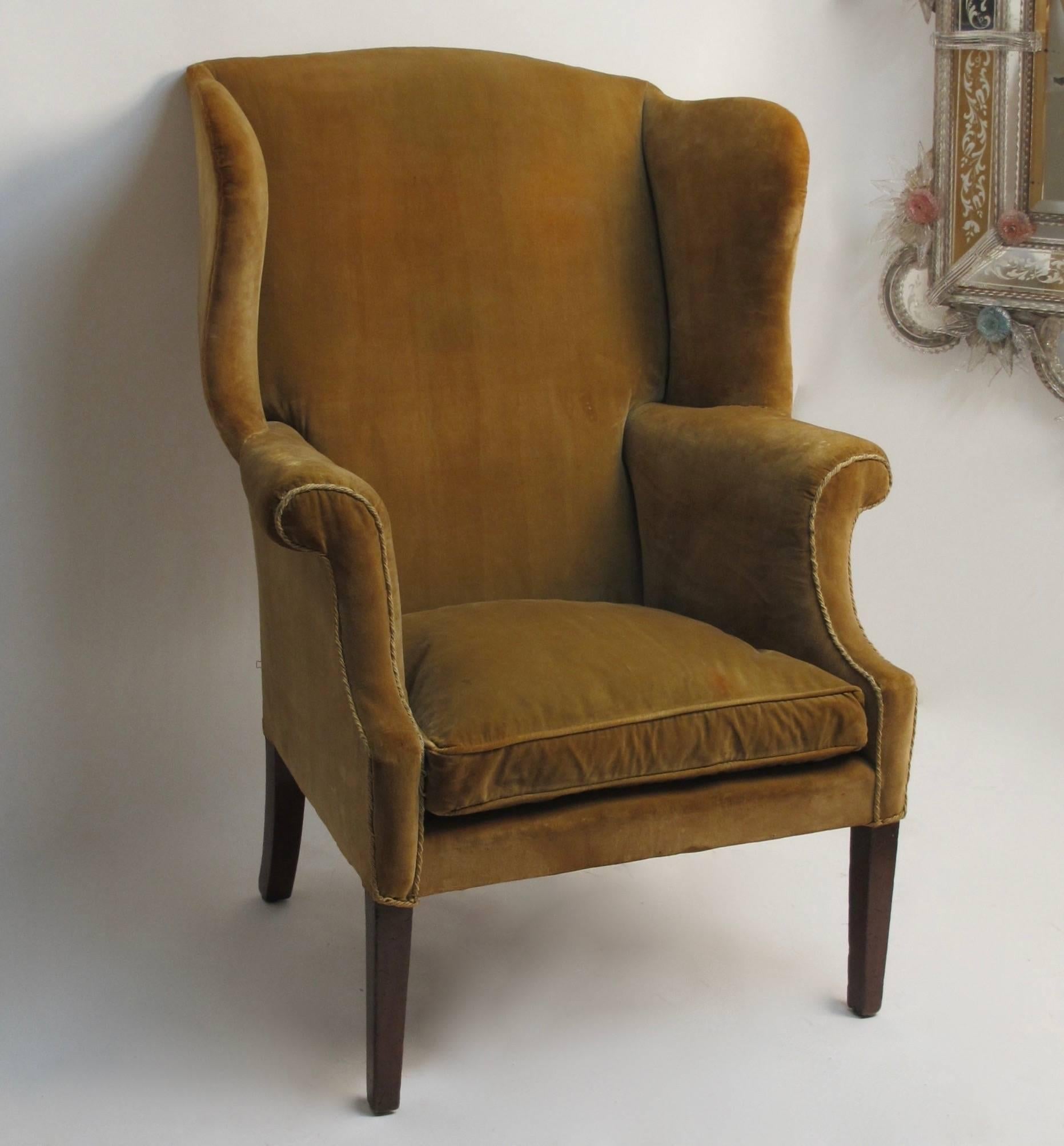 A generously proportioned wingback chair with tapering mahogany front legs and rear saber legs. Older upholstery shows signs of use and age. American, 18th century.