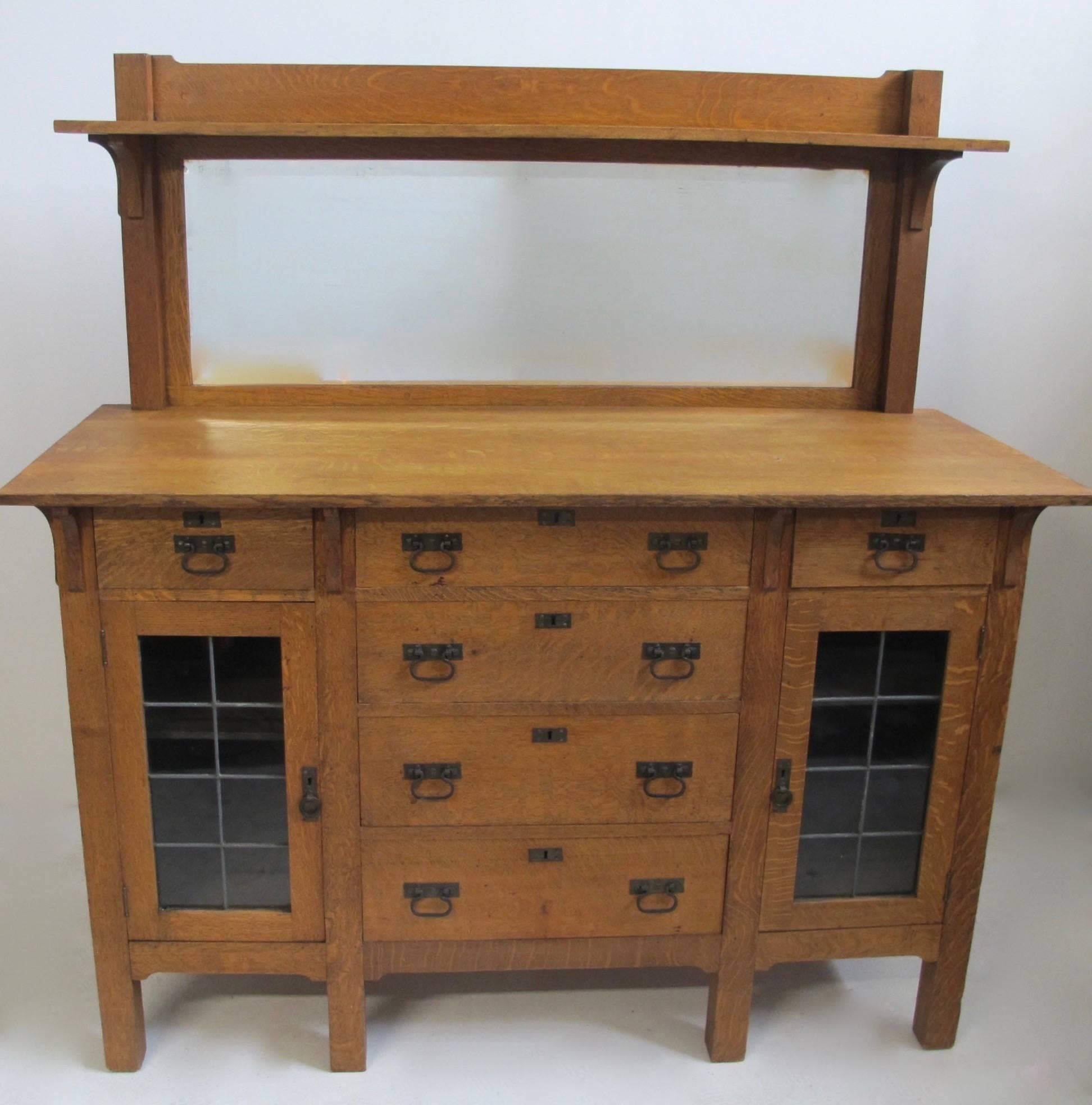 Mission oak sideboard in the Arts and Crafts period design. Having a pair of glass cabinet doors, each having a single adjustable shelf inside, all original hand-wrought iron hardware and beveled mirror back. American, circa 1900.