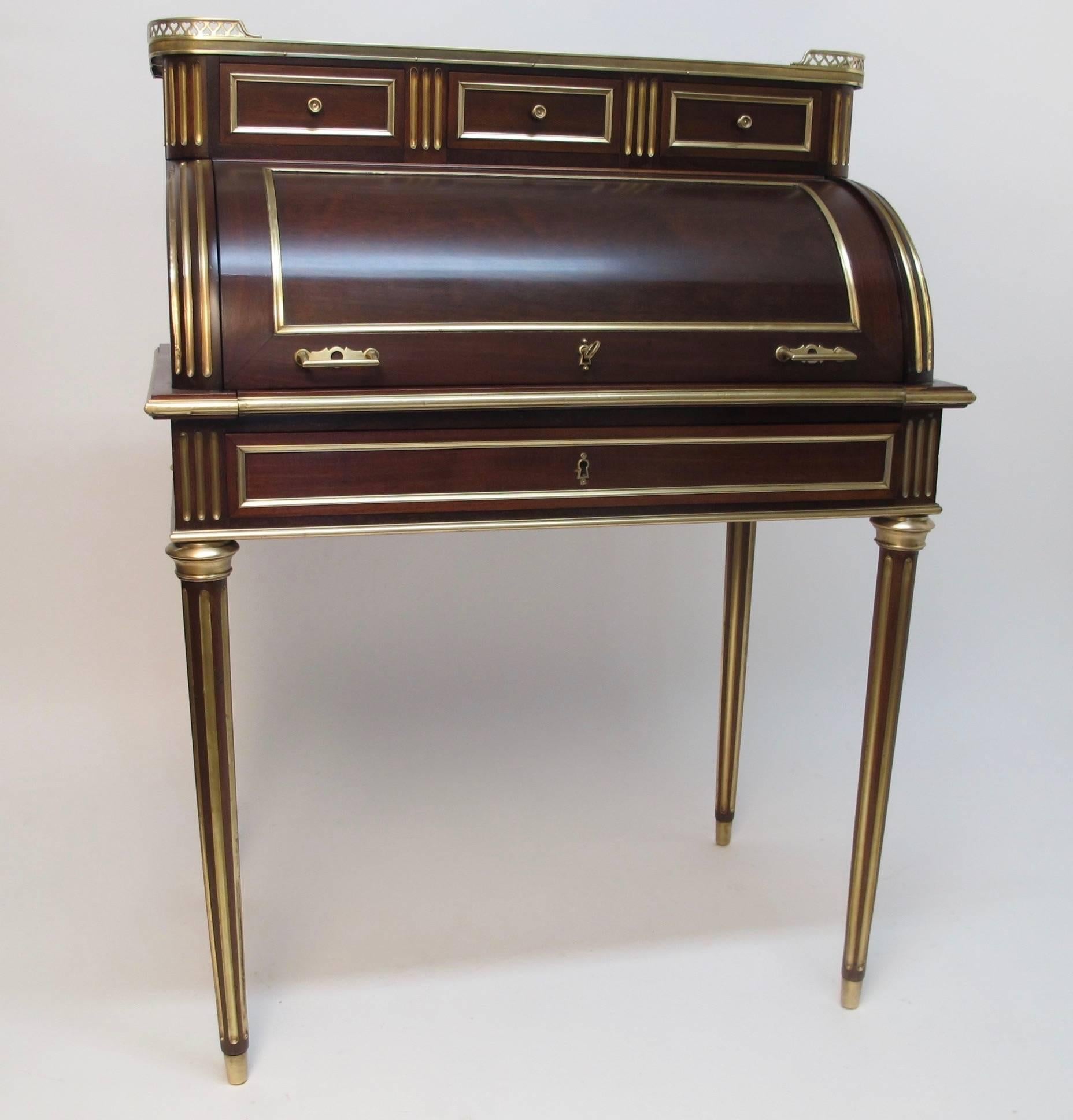 Mahogany cylinder shape desk with brass gallery around inset leather top above three short drawers. Roll front opens to reveal leather pull-out writing surface. All moldings of brass and inlaid brass on the fluted legs, France, circa 1870.