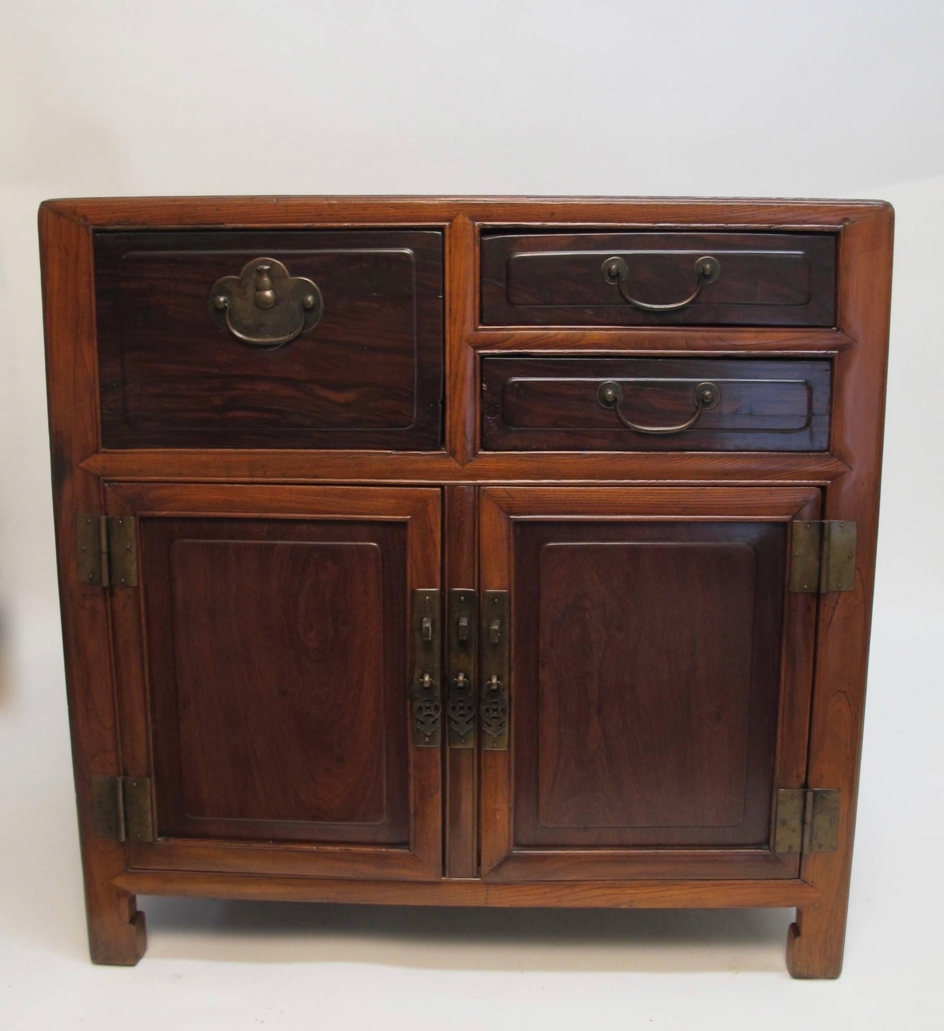 An usual elmwood and rosewood Chinese cabinet. Having an inset rosewood panel on the top, doors and drawers of rosewood, and the body of the chest is Chinese elmwood. Original brass pulls and hardware. Interesting molding detail around the entire