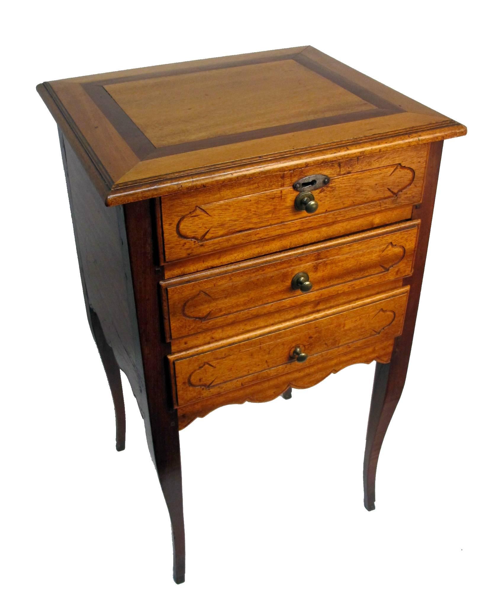 Wonderfully charming bedside table of satinwood mixed with mahogany standing on cabriole legs (curving legs) ending in notched foot. Three drawers with carved fronts and brass pulls. The top drawer with interesting steel cut escutcheon plate (the