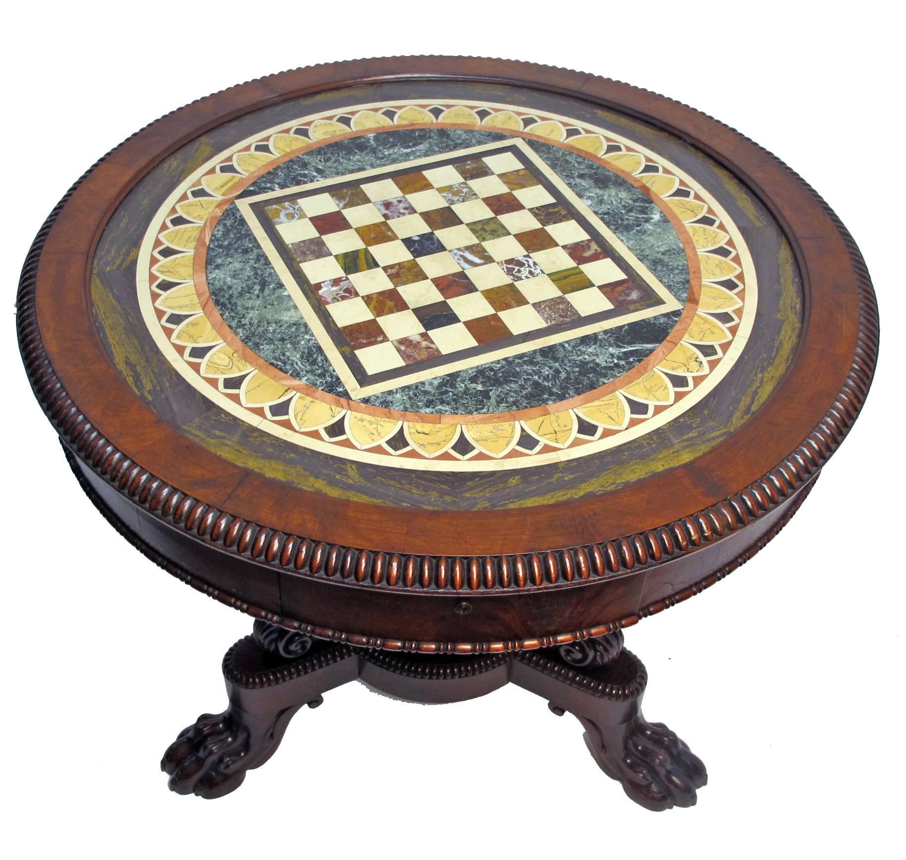 Regency period mahogany game / center table with inset Pietra Dura (stone specimen) marble chess board top. Having two drawers on either side, and a boldly carved base ending with paw feet. 
Of exceptional quality, in remarkable antique