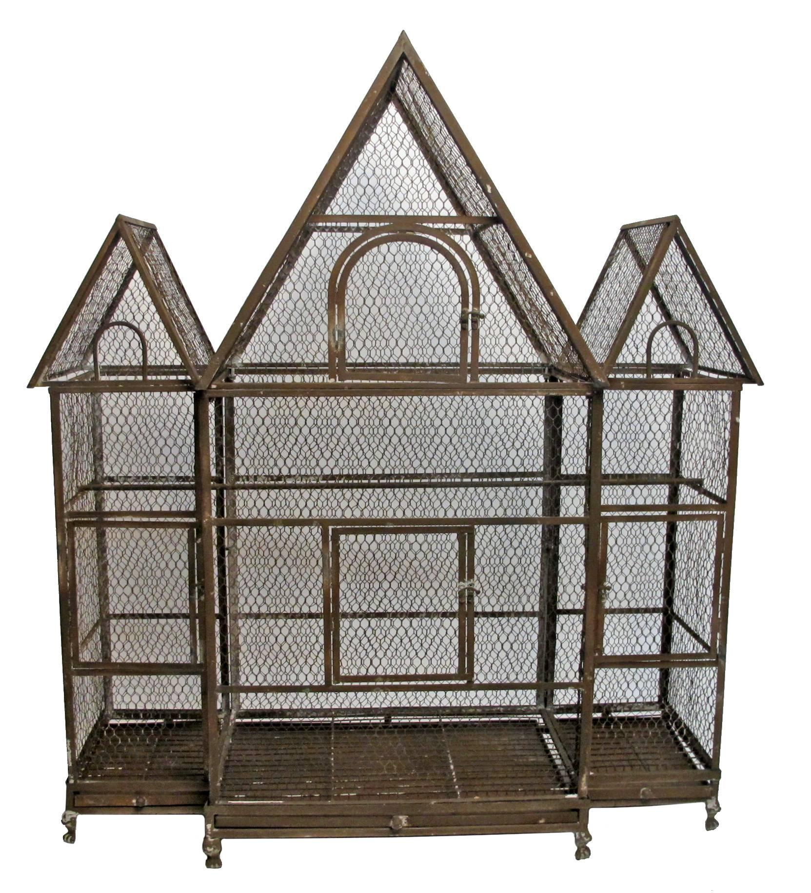 A very large architectural in shape aged tin birdcage with three slide out drawers at the bottom and having remnants of old paint. American, early 20th century.