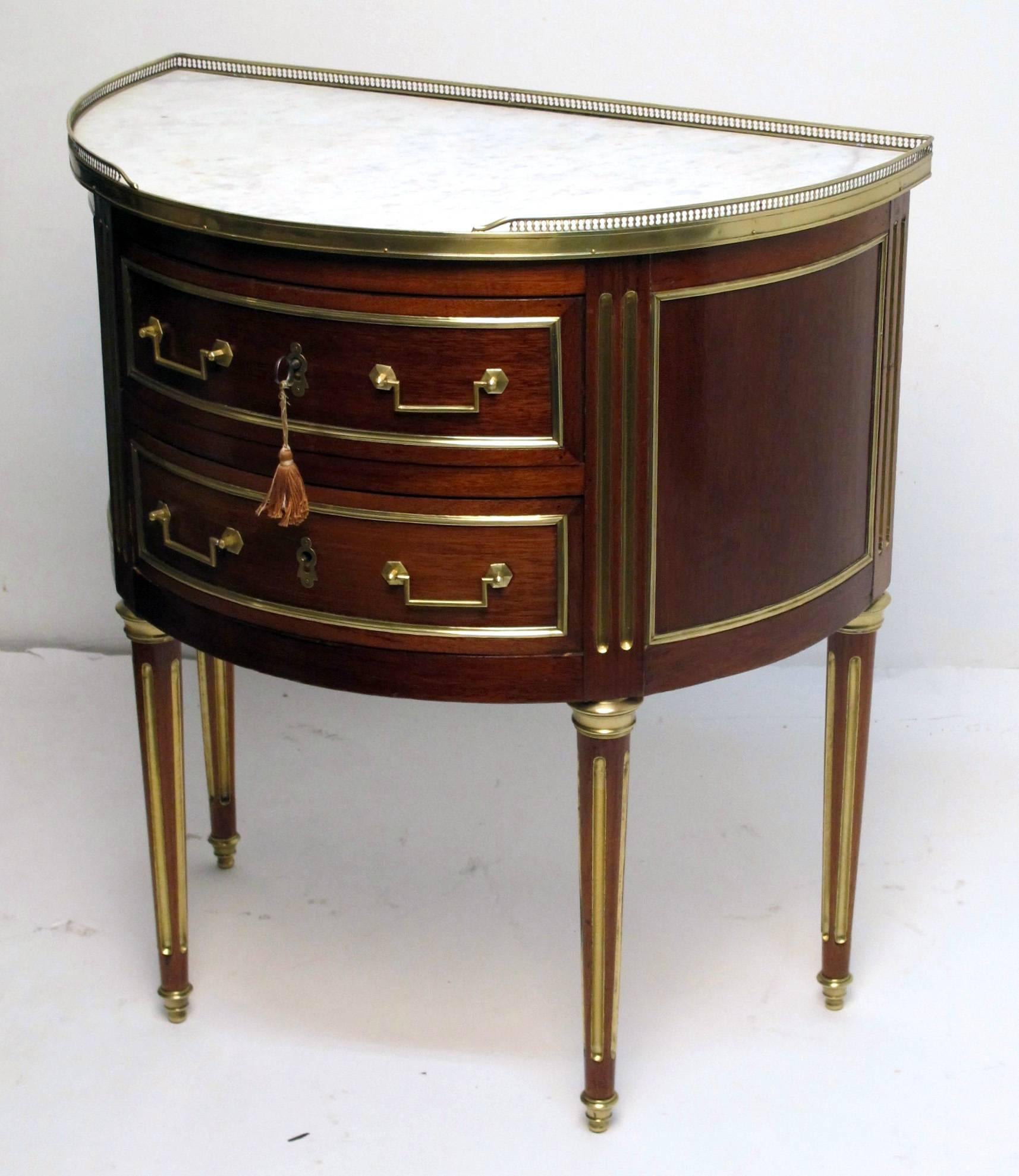 A Directoire period (1789-1804) mahogany demilune side table with a marble top and two drawers. Having brass trim, gallery, hardware and brass inlay on the fluted legs, France, late 18th-early 19th century. Original marble top has a small older