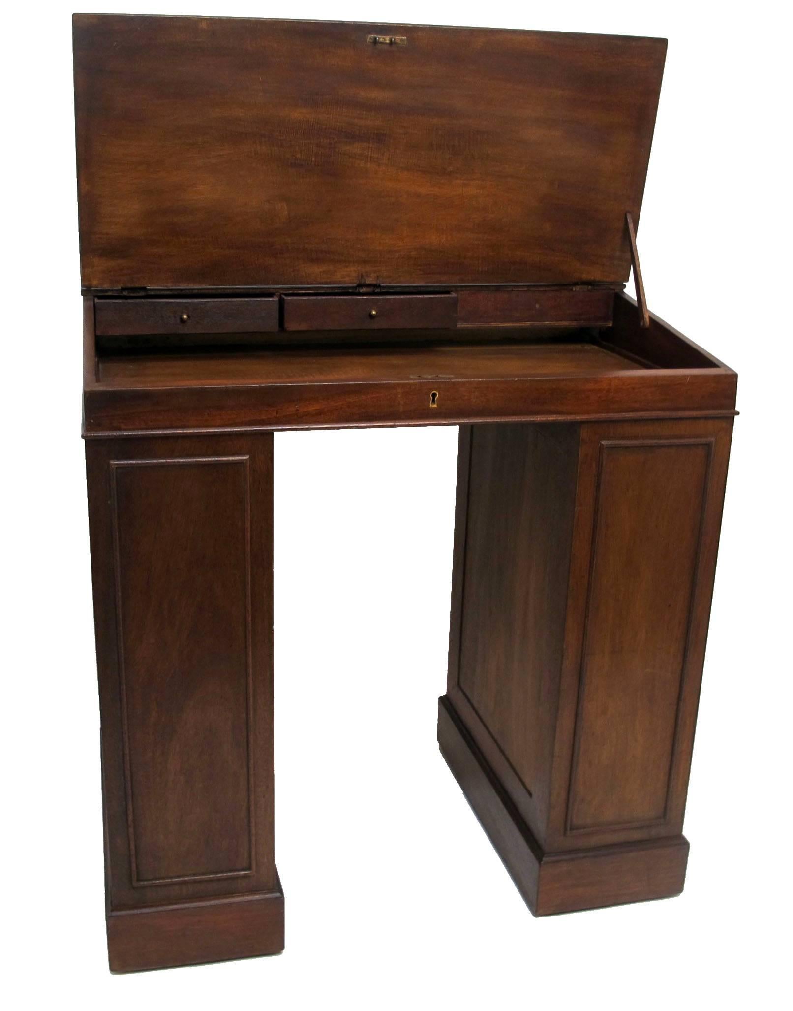 Mahogany ship's desk with inset black leather sloped writing surface, opening to reveal a fitted interior with three drawers and separate drawer for ink and quills. Flanked on either side by bookshelves, England, circa 1880.