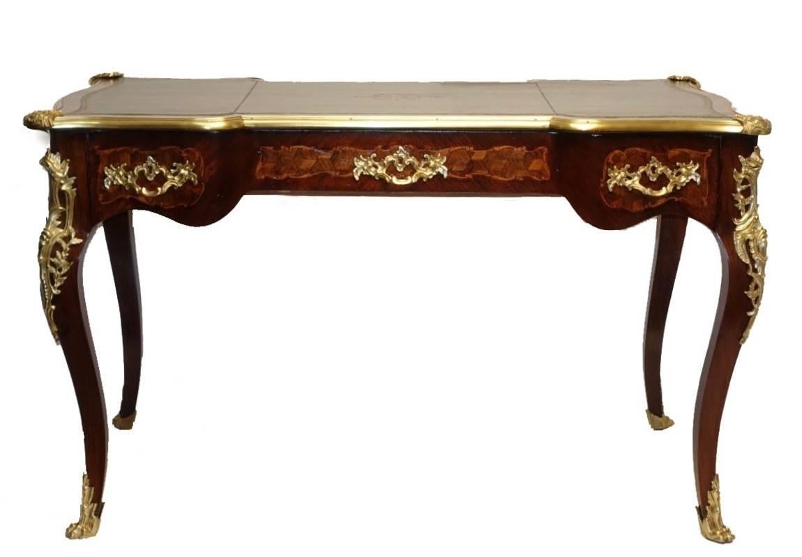 Serpentine shape Louis XVI style desk inlaid with mahogany and rosewood, having robust brass mounts, and inset green leather writing surface with gilt tooling detail. Has two short drawers flanking a wide center drawer, the opposing side with false