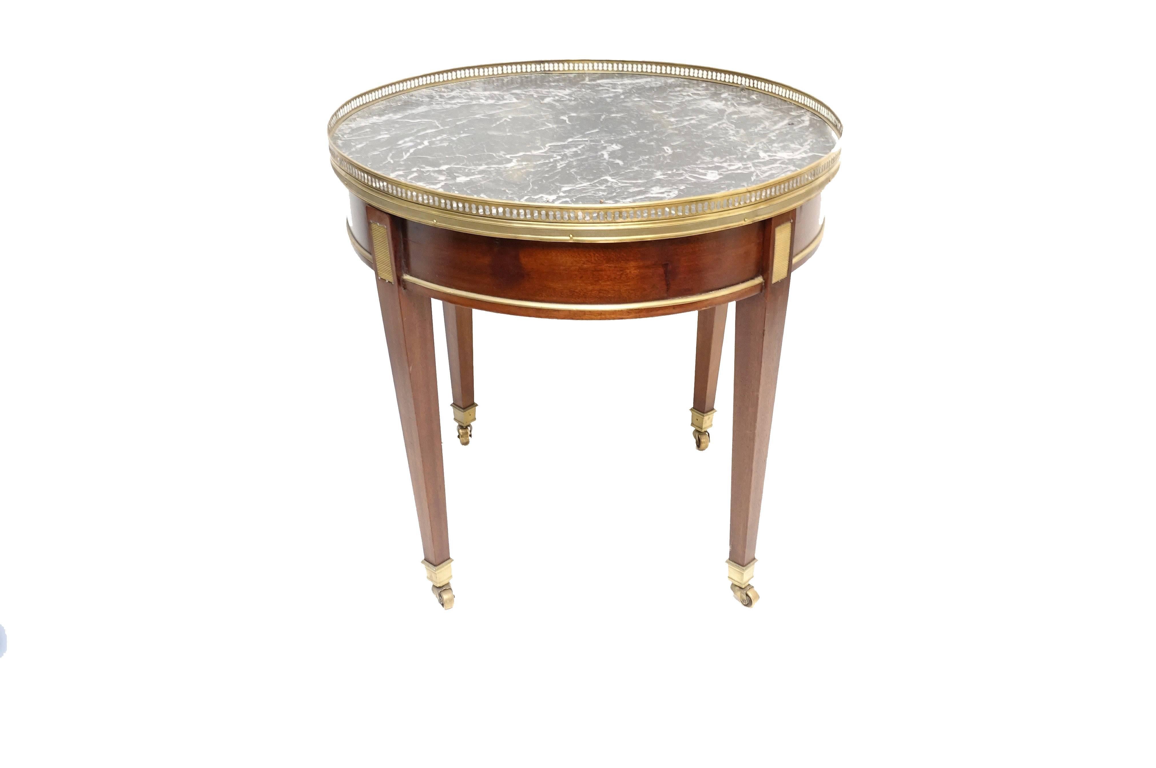 Louis XVI style mahogany bouillotte table with veined gray and white marble top. Having a brass gallery and moldings, with ribbed brass fillet inlay and tapering legs ending in brass sabots with casters. France, circa 1870.