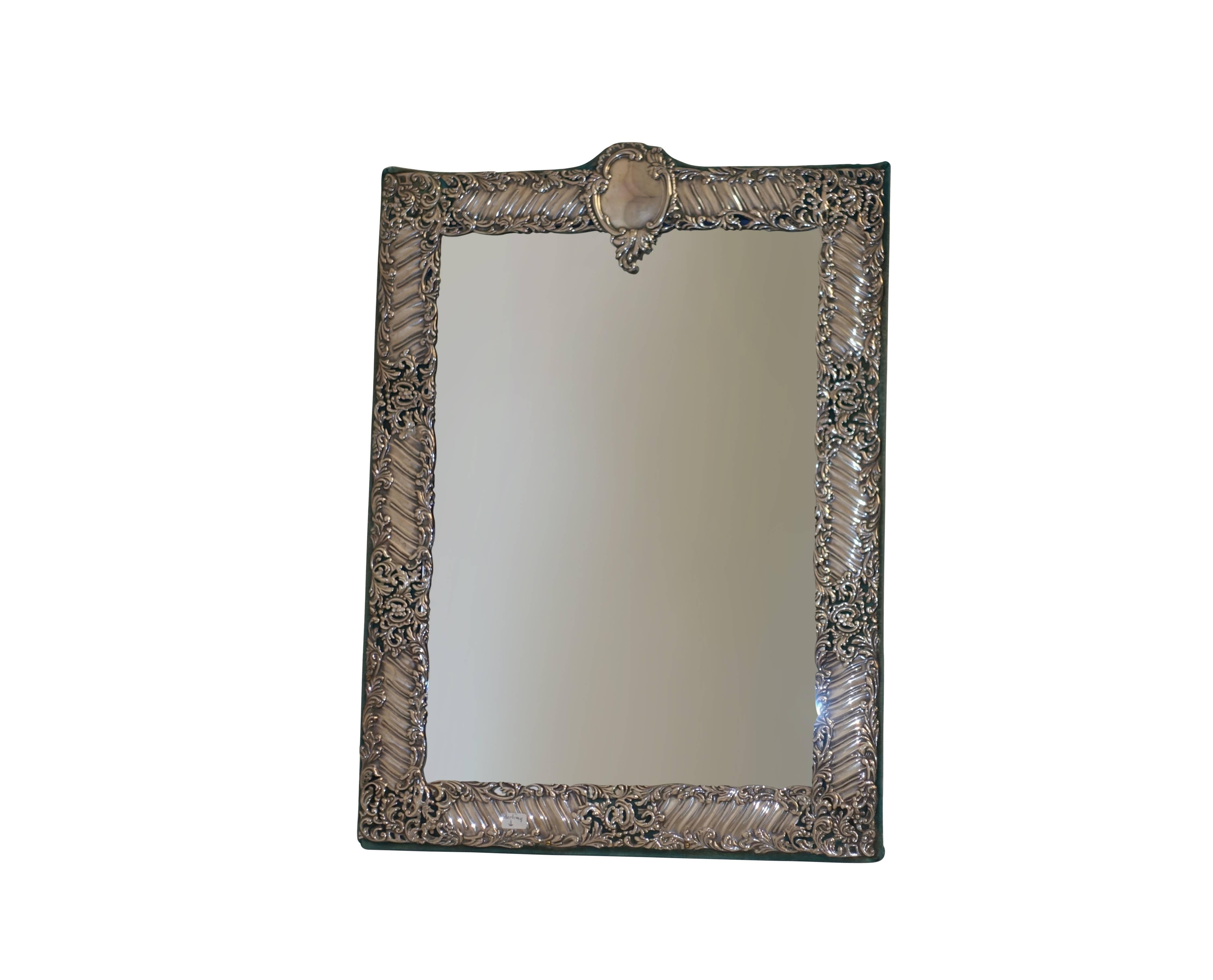An elaborately embossed sterling silver tabletop mirror mounted on turquoise velvet backing, and having a beveled edge mirror glass. The centre cartouche is un-monogrammed. English hallmarked silver. The inner sight on the frame measures 13.5 inches