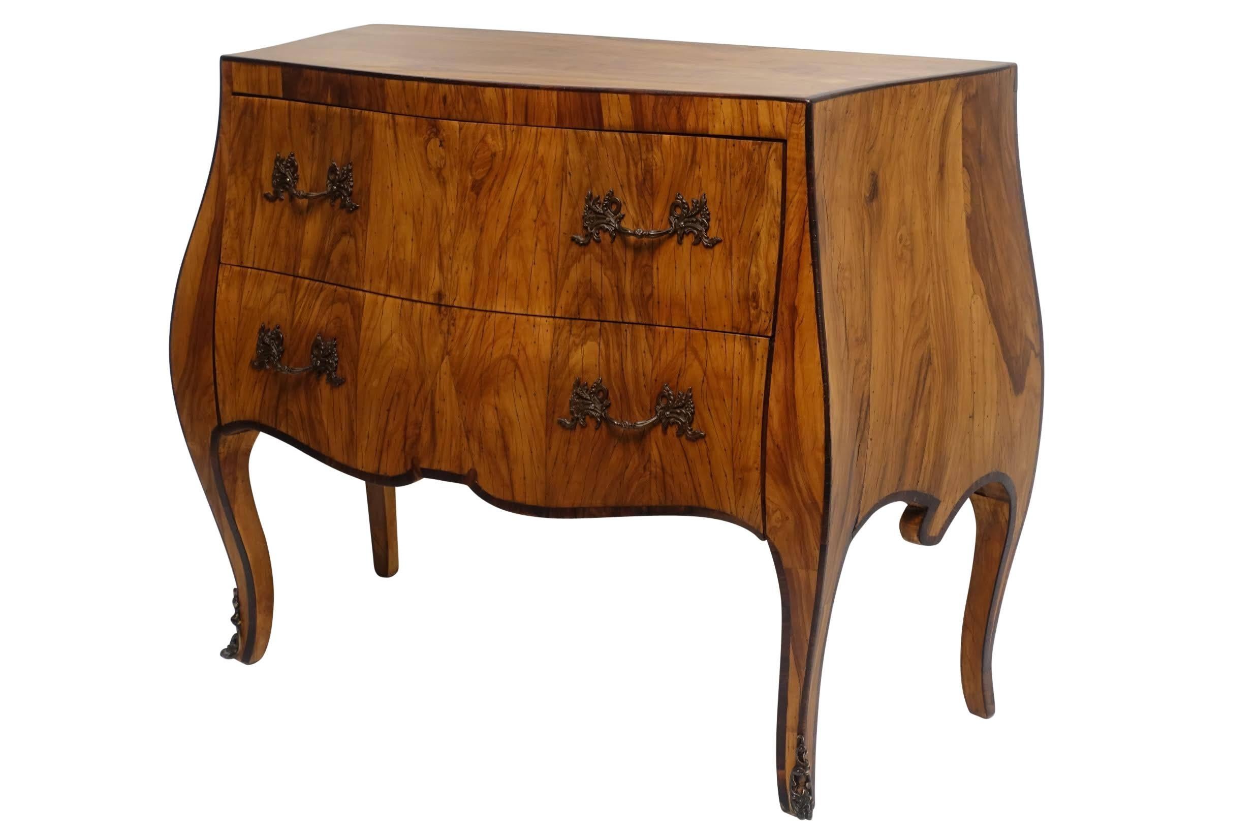 Beautifully bookmatched walnut veneered two-drawer Bombe style chest of drawers. Having brass pulls, and standing on cabriole legs ending in brass mounted feet. The overall lines of the body are accentuated with ebonized inlay, Italy, 1960s.