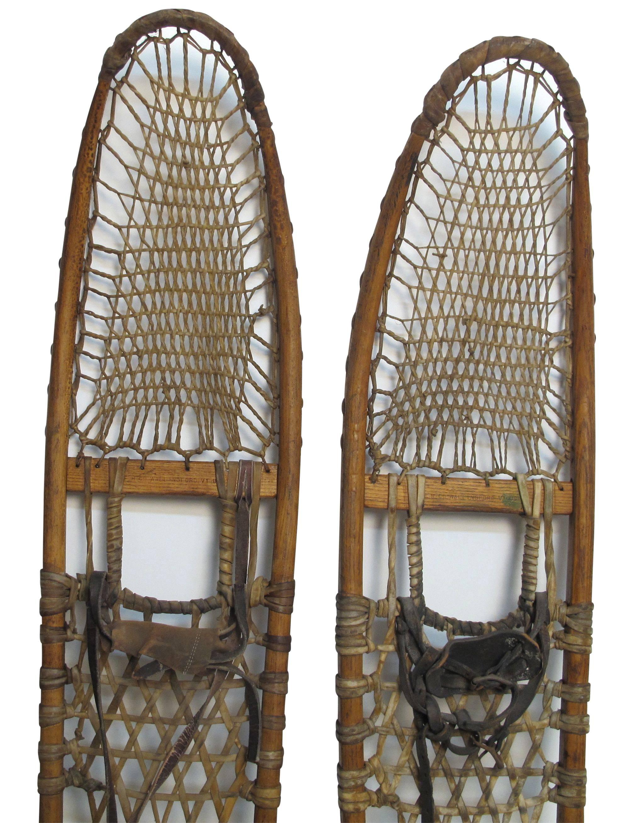 A large pair of antique snowshoes having a wood frame, rawhide webbing and leather straps. Marked E. H. Co. Wallingford Vermont US.