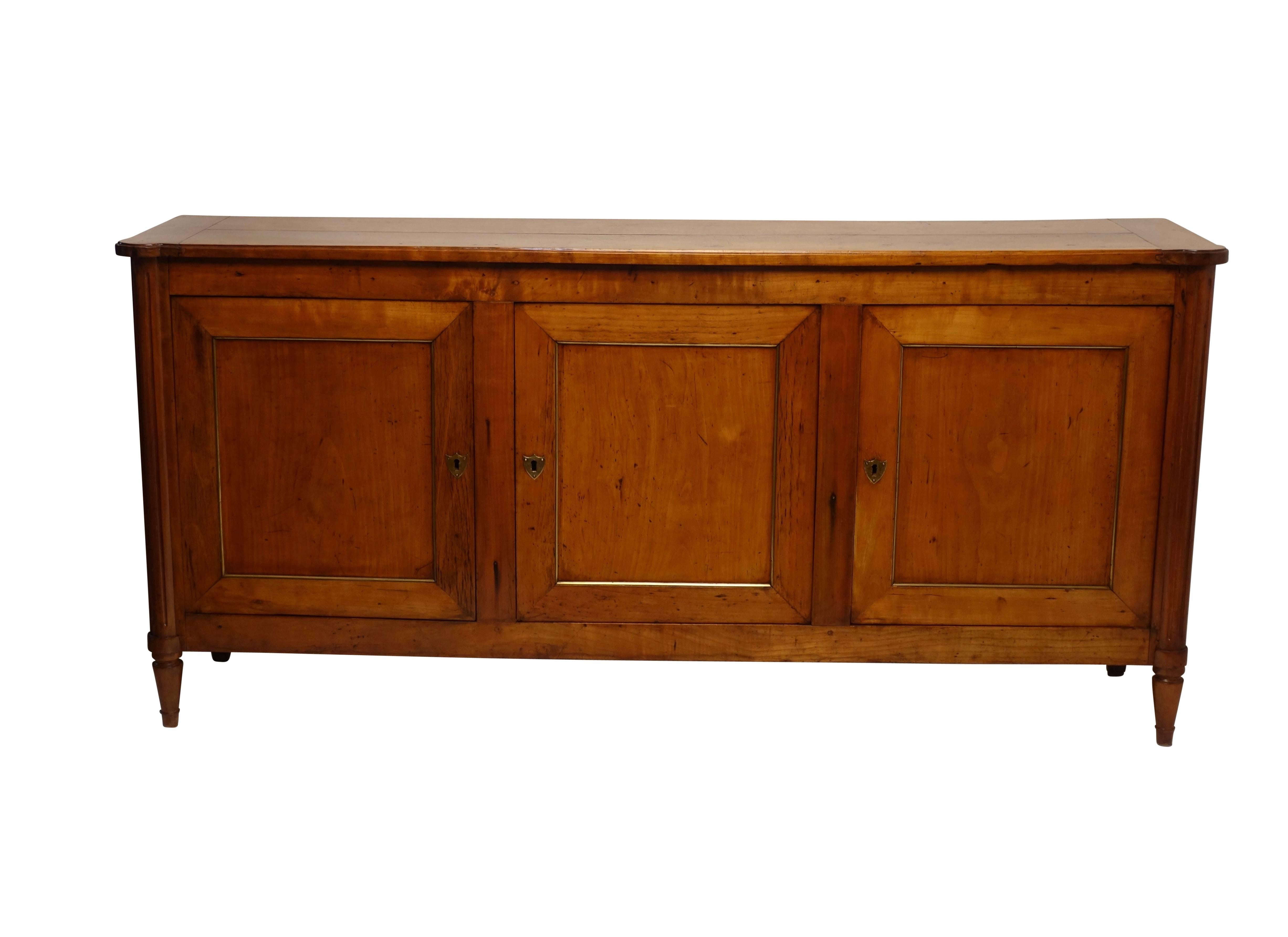 Unique size Directoire period buffet enfilade. Having a shaped top above three brass trimmed recessed paneled doors flanked by fluted column supports, standing on turned tapering legs. Exceptional rich cherrywood color throughout and interior fitted