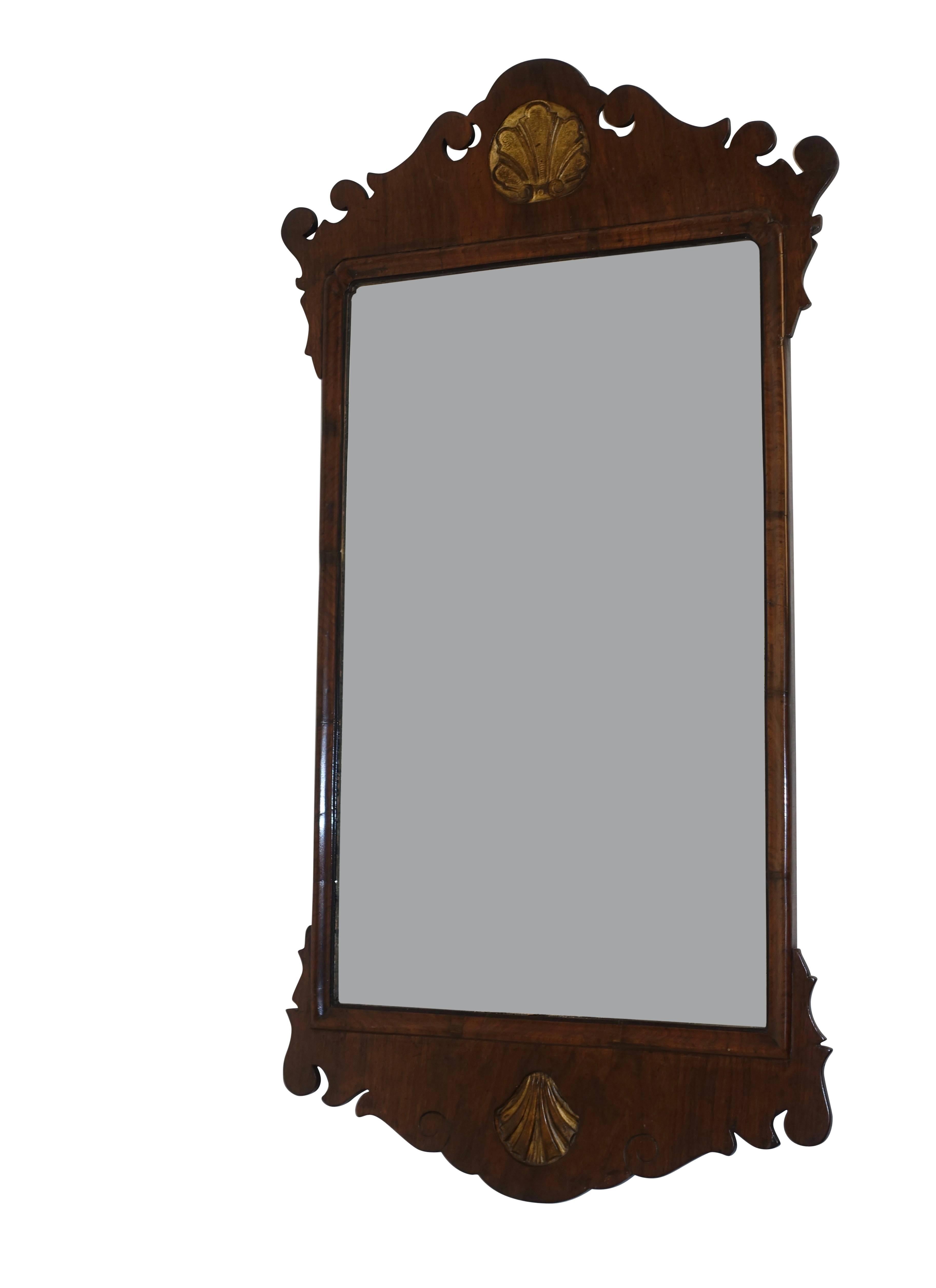 A George III carved walnut mirror having a carved and gilt stylized shell design at the top and bottom, England, circa 1800. 
Old mirror shows some expected light and minor spotting.