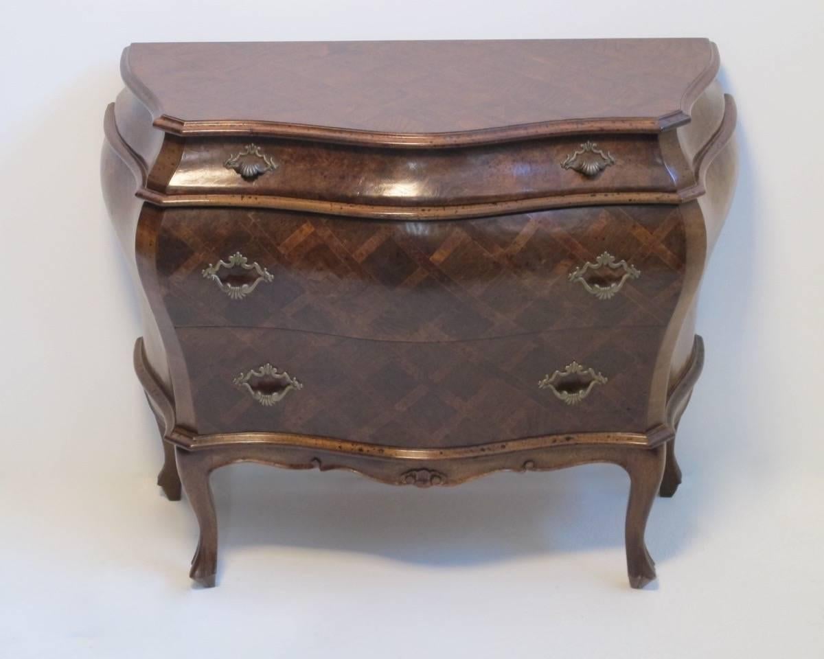 A Rococo style three drawer Italian bombe commode or chest of drawers with inlaid cross hatch design, sitting on cabriole legs. Italy, mid 20th century.