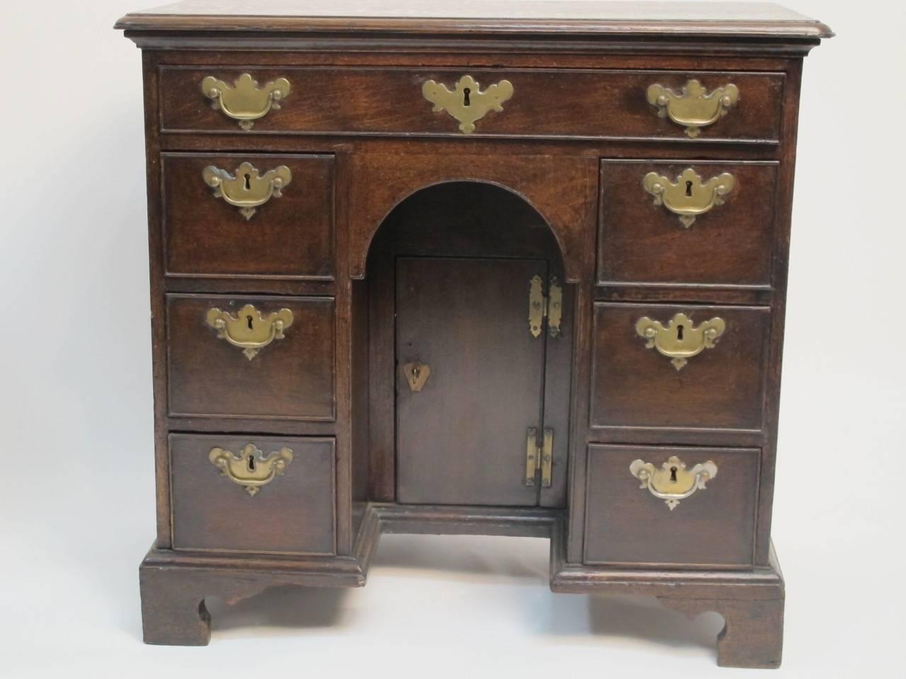 George II oak desk or dressing table with a single drawer above three short drawers flanking an arched center kneehole with cabinet door, brass hardware, England, early 18th century.