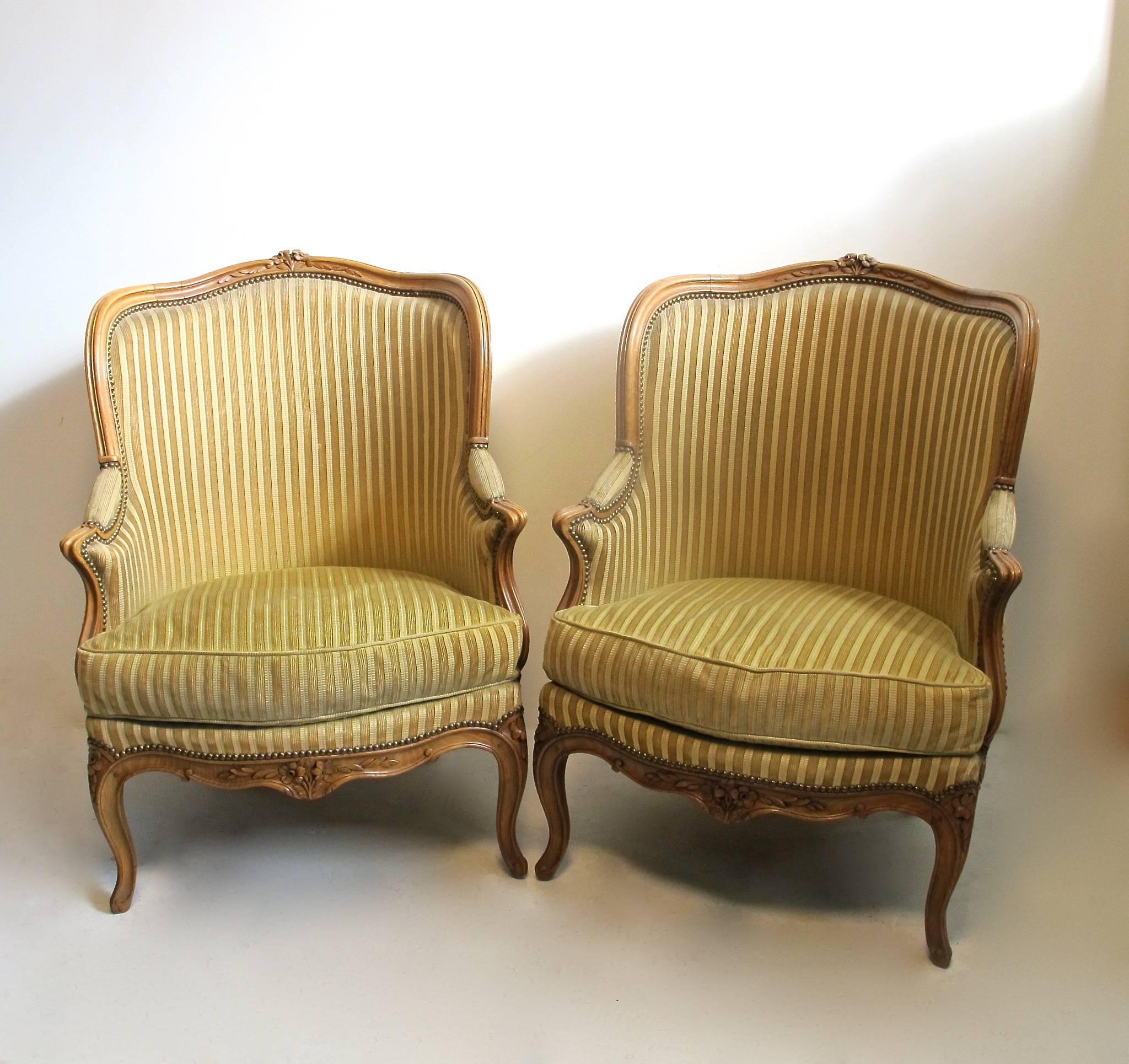 A pair of carved Beechwood and upholstered bergere chairs. Finely crafted with mortise and pegged construction in the manner of 18th century technique. Vintage cut velvet upholstery (shows wear) and down filled cushions.