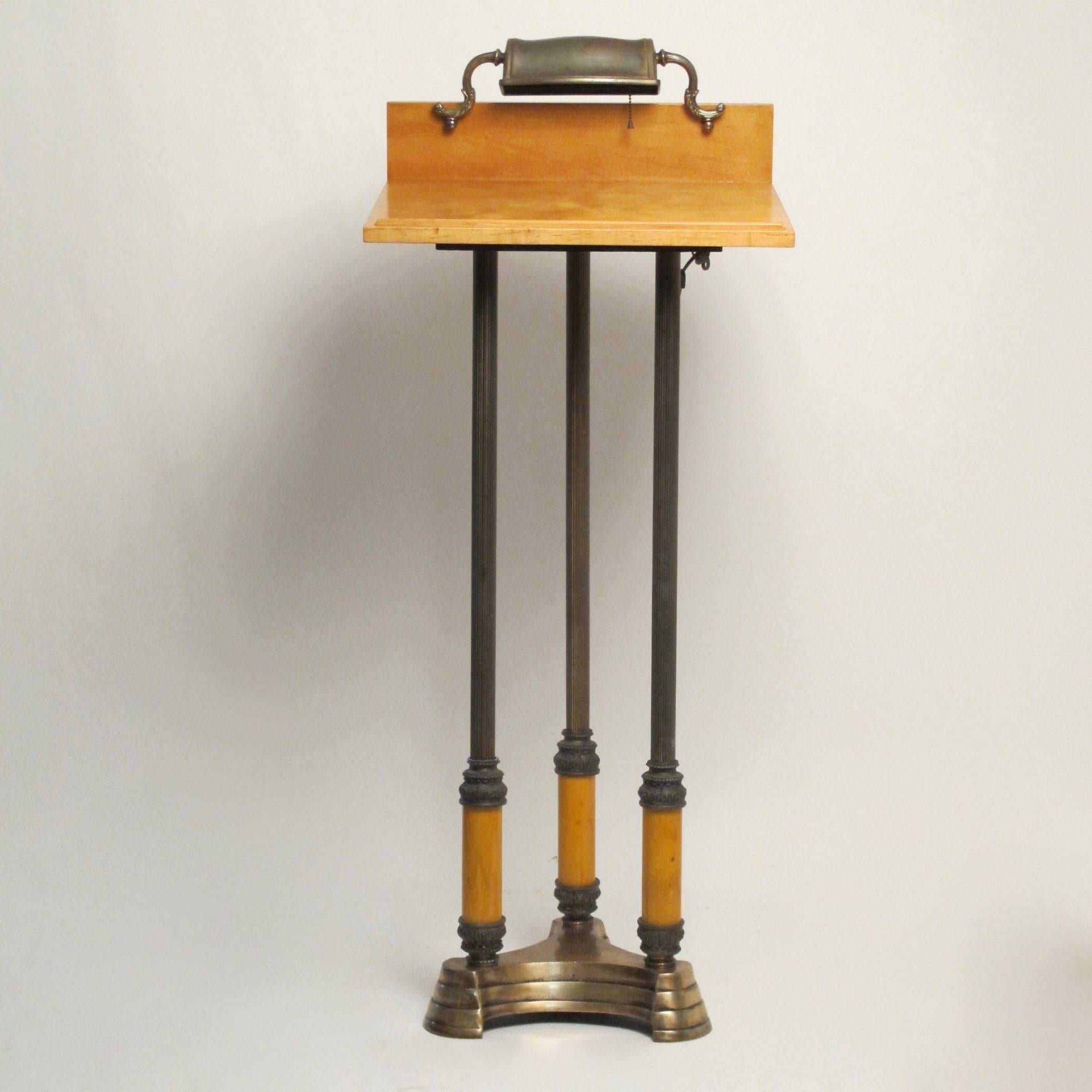 Neoclassical style lectern with brass adjustable light. Steel and bakelite with three ribbed column supports, standing on a bronze plated stepped base.