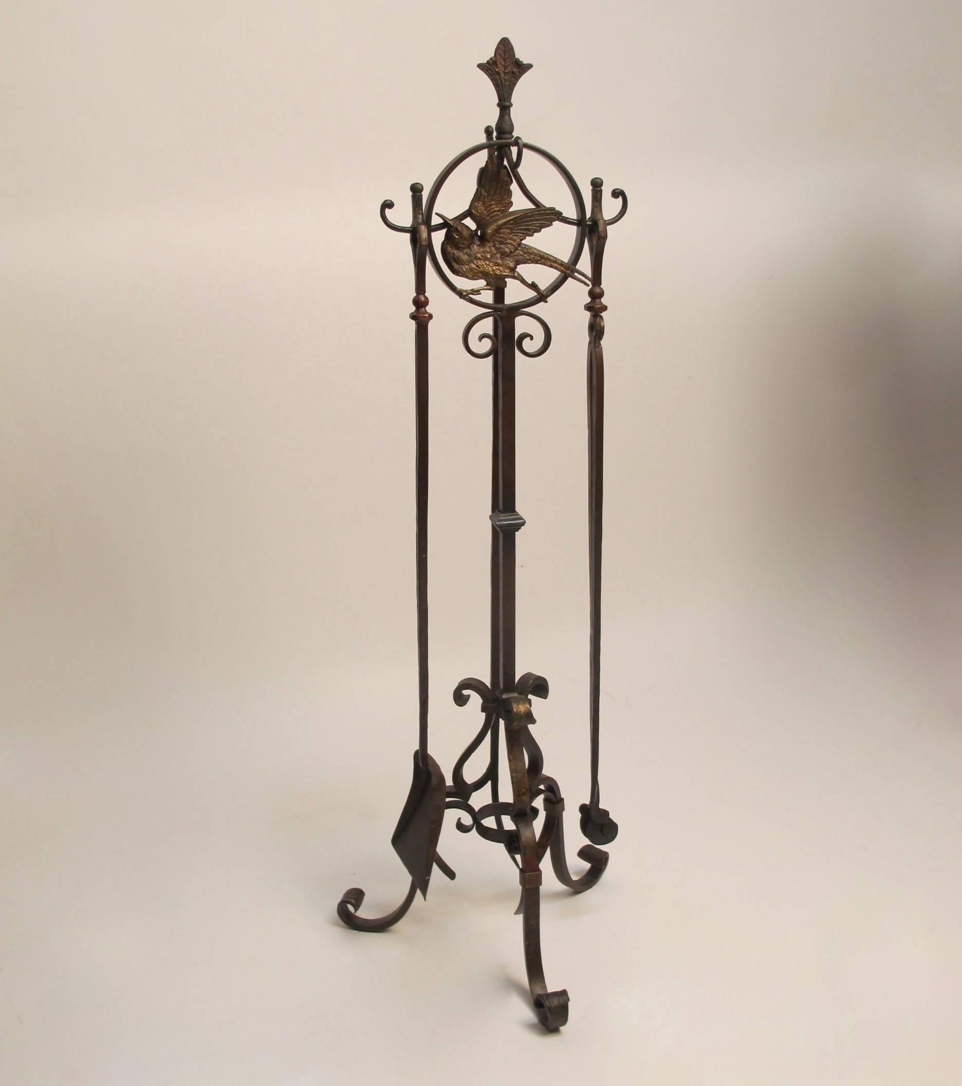 Arts & Crafts period hand-forged iron fireplace stand and tools with cast brass bird detail, retaining much of the original paint. Four tools consisting of a poker, tongs, shovel and a brush.