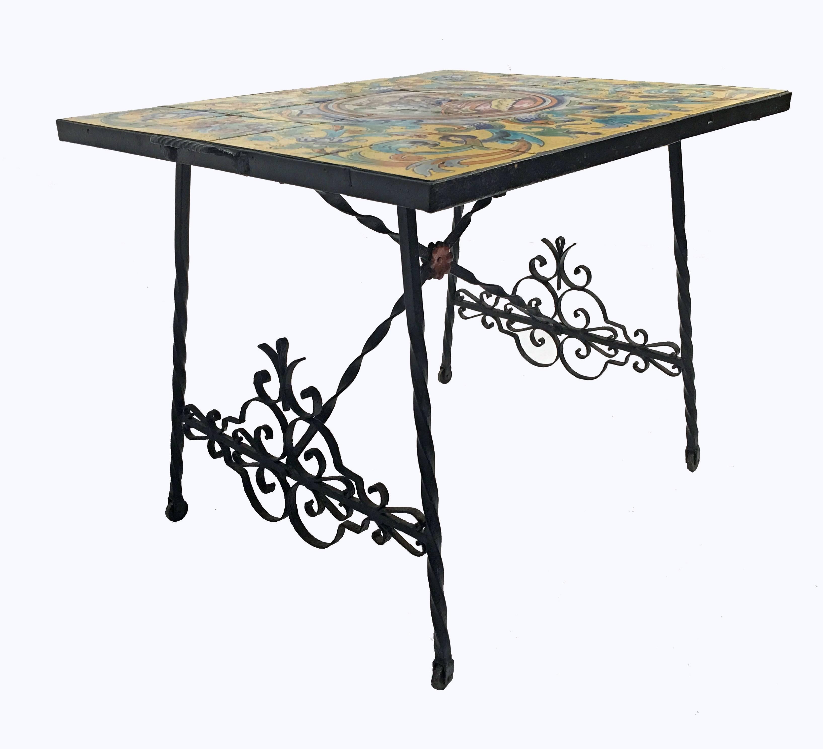Brightly decorated tile top table rests on hand-wrought iron legs, handles and ornamental stretchers and trusses. Legs rest on functioning iron wheels. Artisan crafted ceramic tiles originating from Ceramica Santa Ana in Triana District Seville,