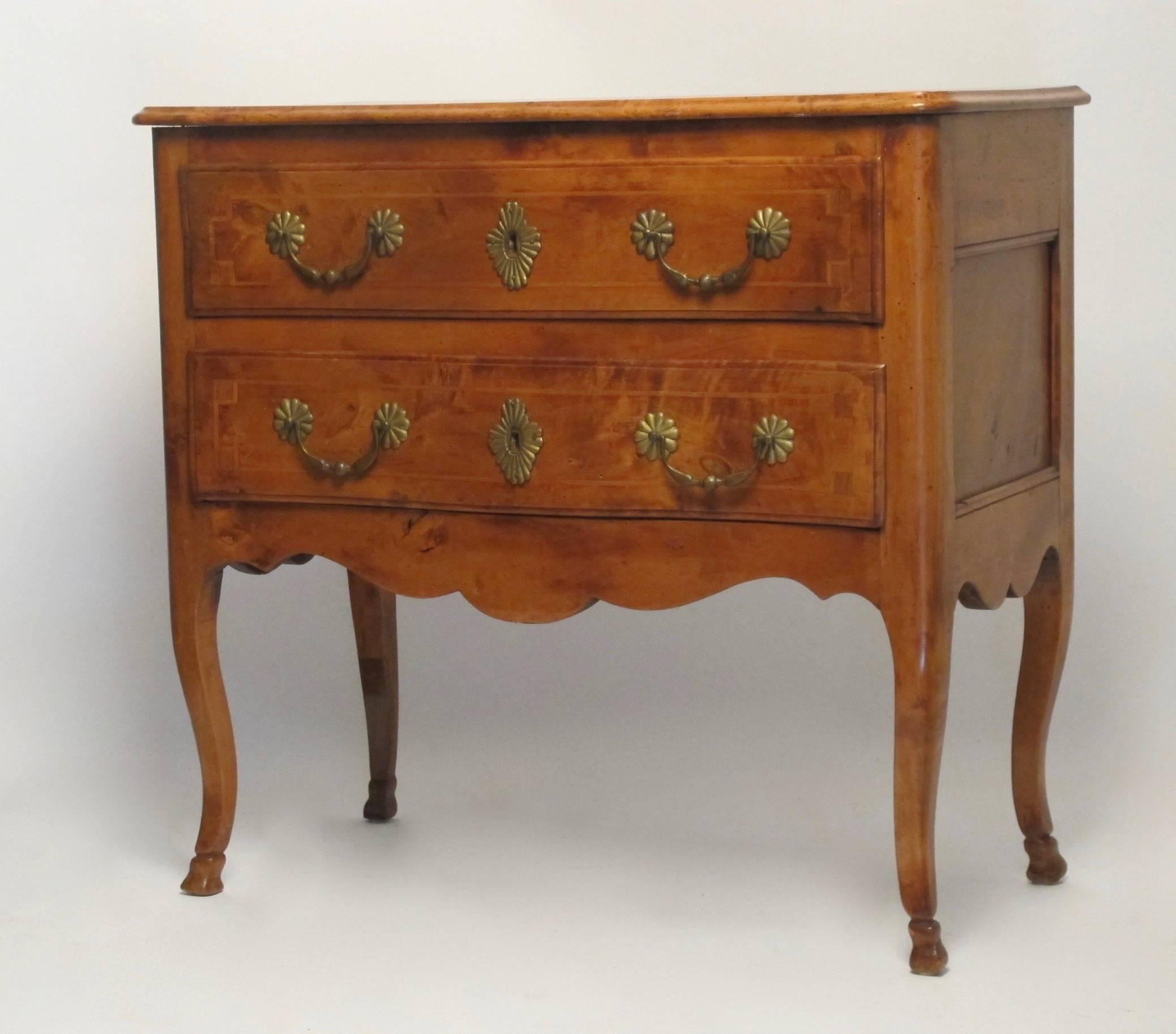 An unusual petite size applewood chest of drawers with shaped top above two satinwood inlaid drawers. Having brass hardware, oval sunburst escutcheons, and supported on cabriole legs ending in carved feet, France, circa 1820.