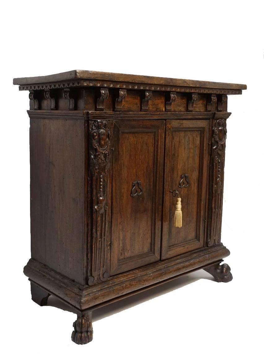 Two-door walnut cabinet with dental moulding around the top being supported by carved corbels, having recessed panel doors with iron pulls, all supported on carved lion paw feet in front and shaped bracket feet in the rear. Italy, 18th century.