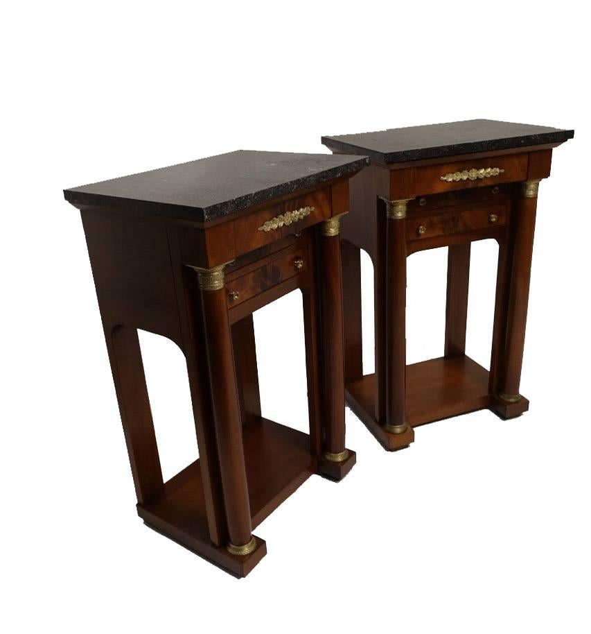 Mahogany Empire style three drawer bedside cabinets. Having black and gray marble above a frieze drawer with two drawers below, flanked by a pair of brass-mounted columns mounted on a plinth base. The back and the sides having an arched opening.