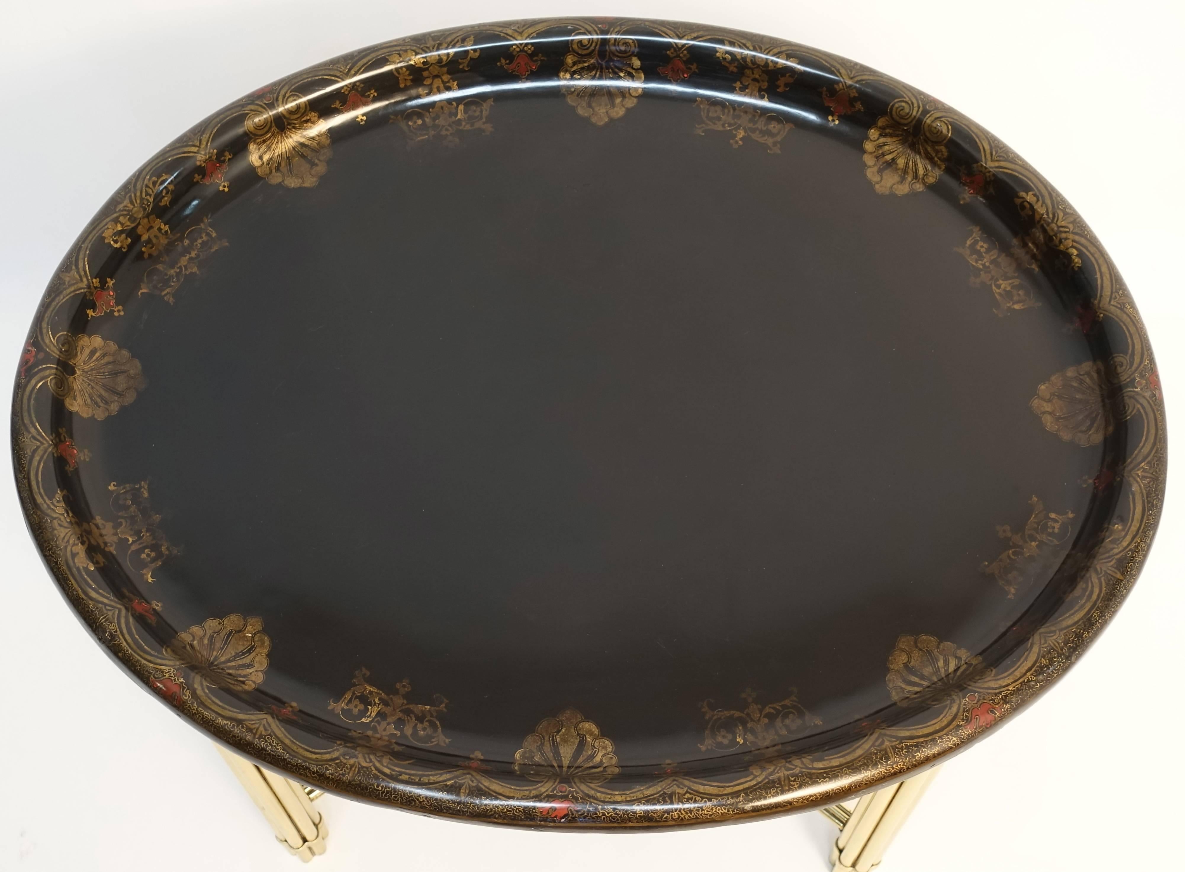Very good oval papier mâché tray with hand decorated border of alternating gilt palmetts and scrolling swags with accents of red mixing with the gilt and black ground sitting on a later faux bamboo brass stand. The paper mâché tray is circa 1830 and