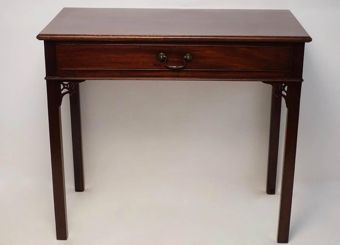 Elegant mahogany serving table or writing table with a single drawer standing on four square legs and having carved fretwork angle supports. England, circa 1800.