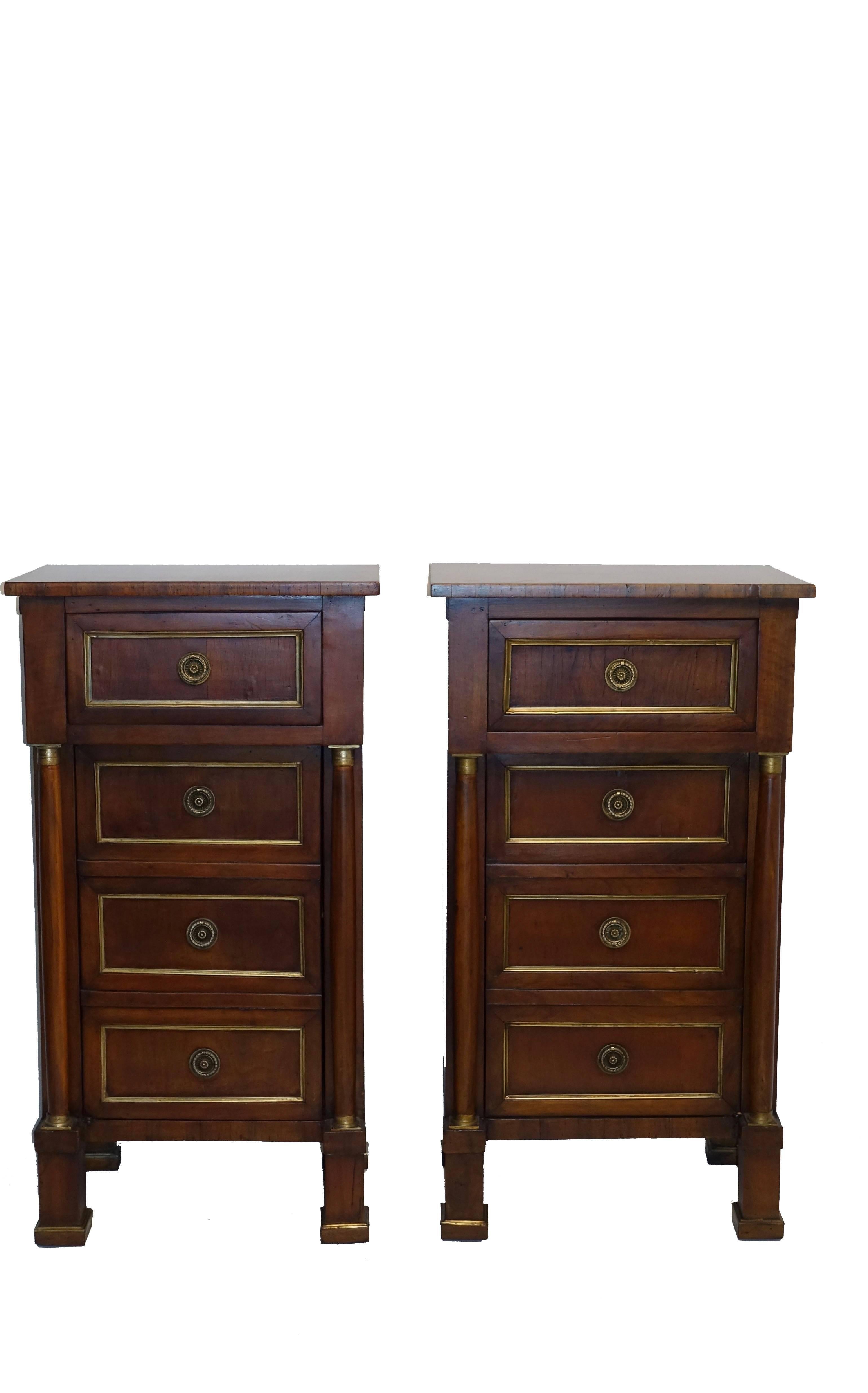 A pair of Empire period walnut comodini, side tables or bedside cabinets. Having a single drawer above three false drawers that open to a cabinet, the door flanked by a pair of columns and brass moulding around the recessed panels, Italy, 19th